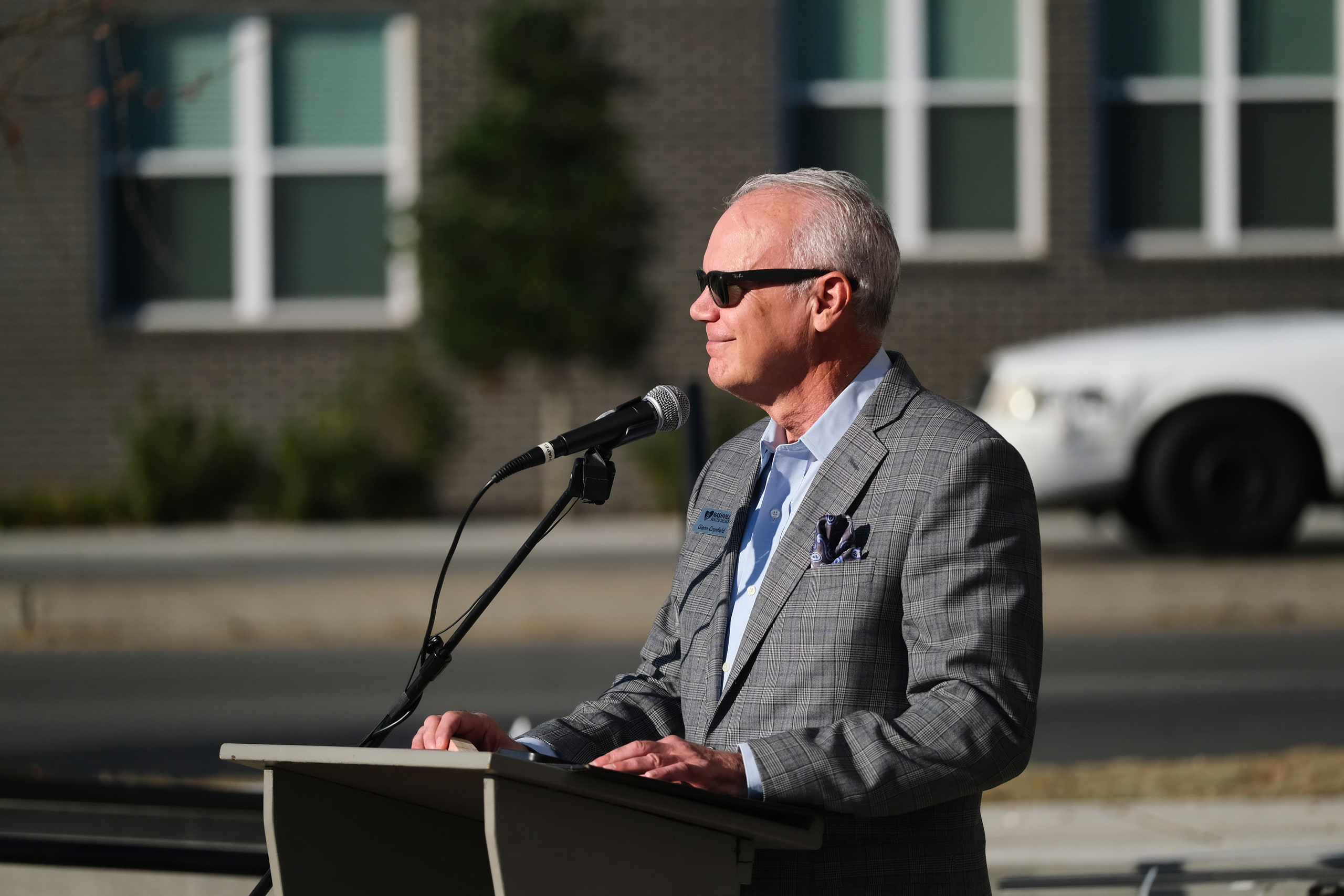 Speaker at the podium, sunglasses, warm at a nonprofit building dedication.