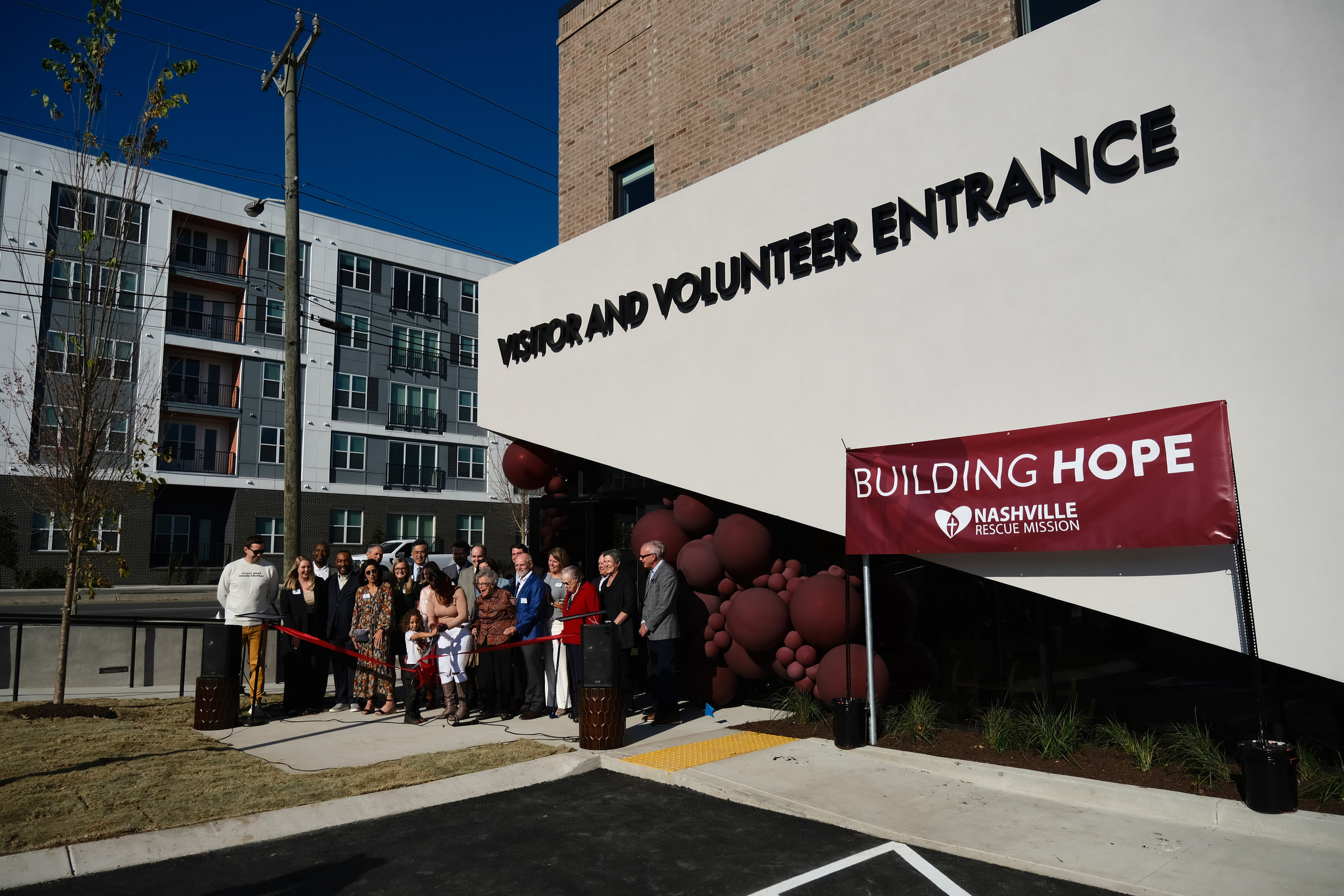 The whole group under BUILDING HOPE, ribbon, wide at a nonprofit building dedication.