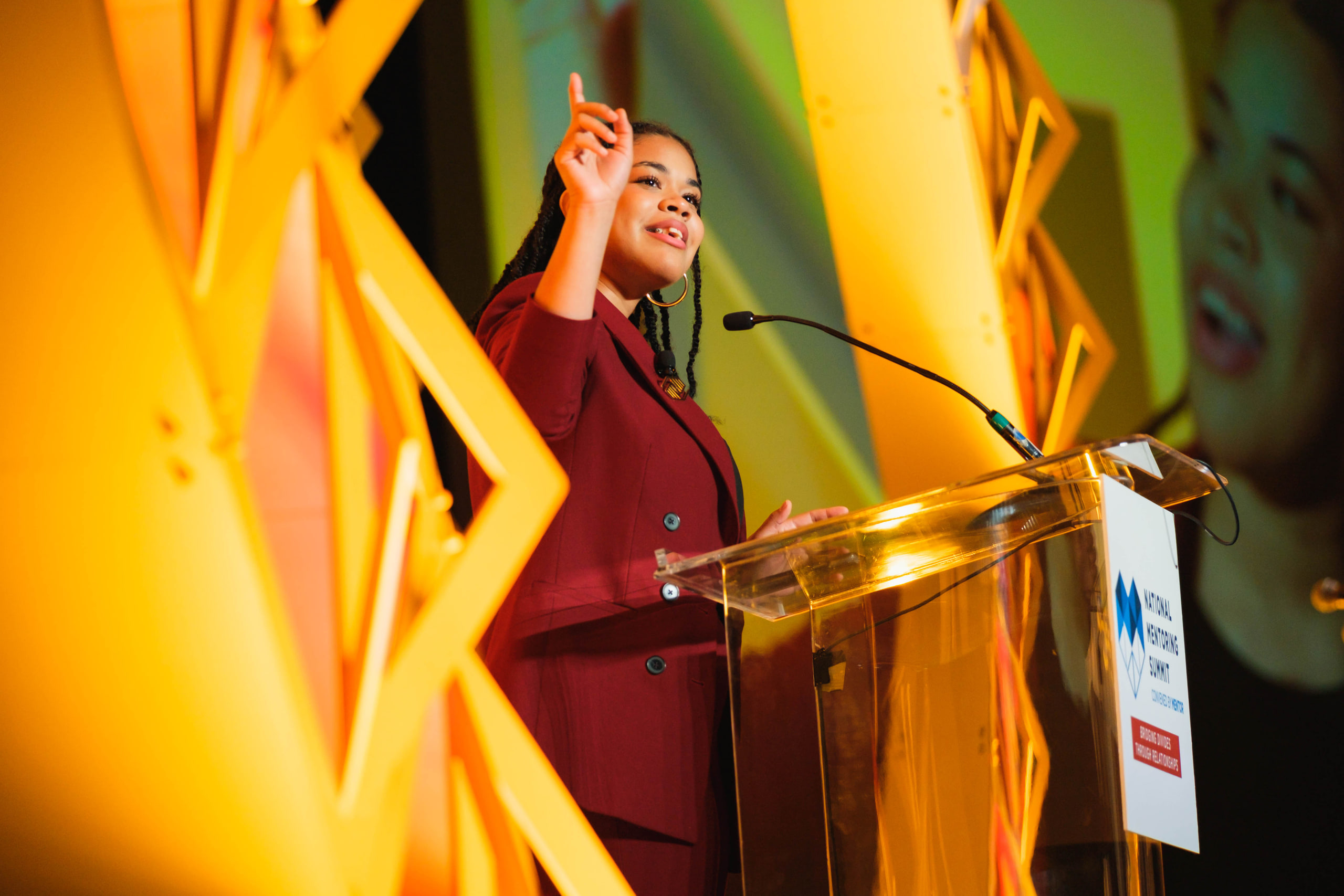Hand raised at the lectern, gold at a national summit afternoon plenary.