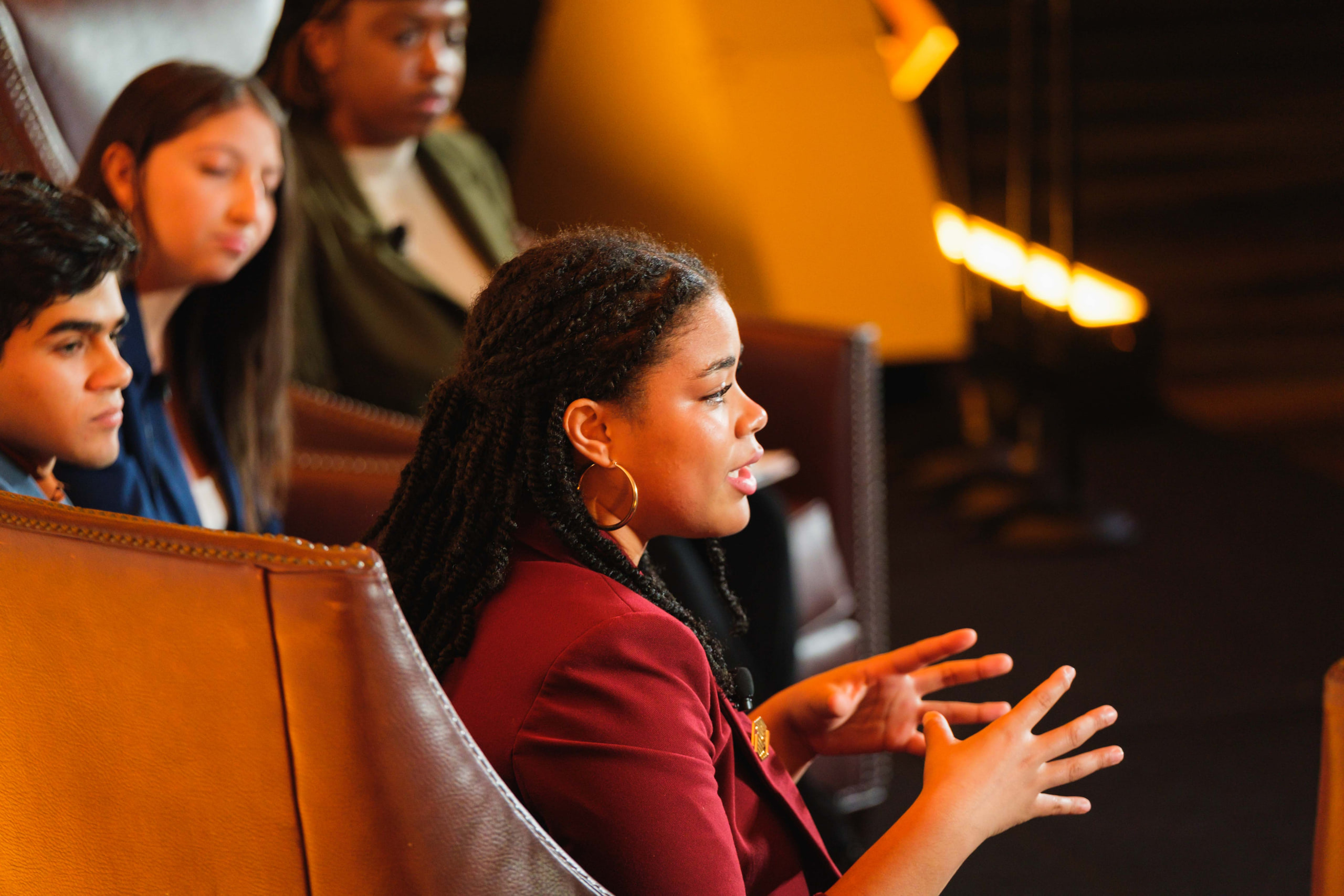 A panelist gesturing from her chair under warm stage light, other panelists beside her.