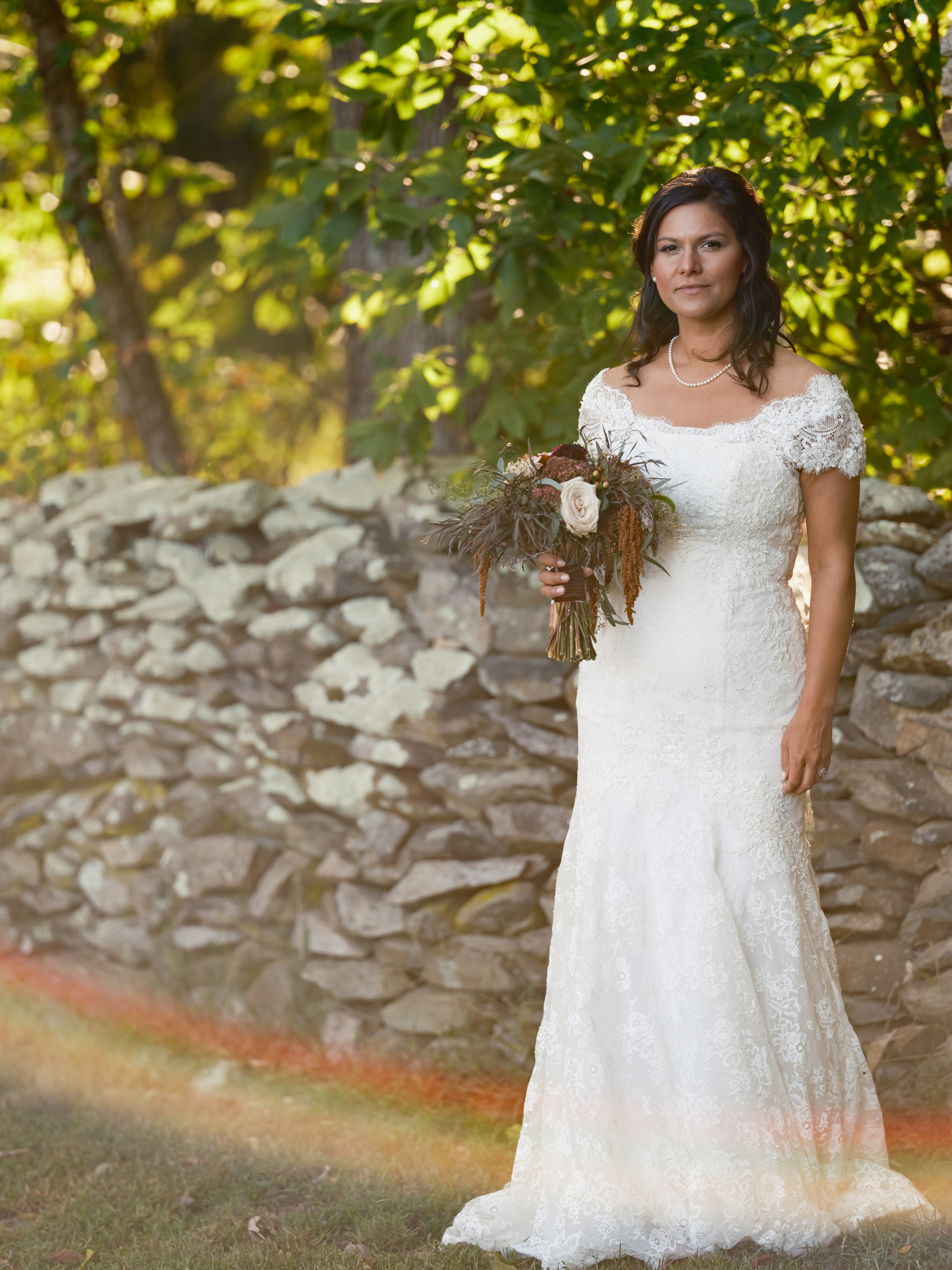 Bride against a stone wall, green surround.