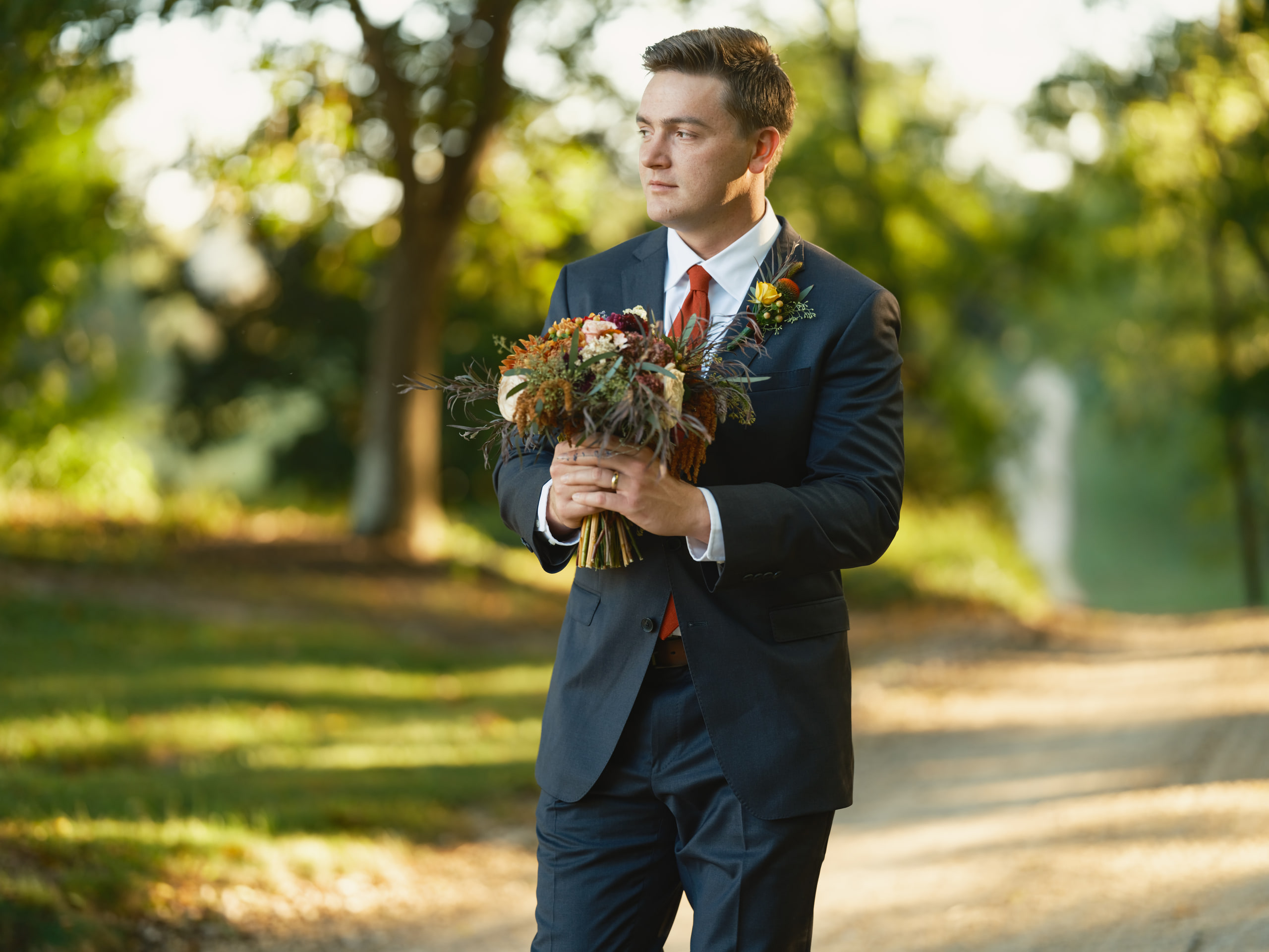 Groom with flowers in dappled light.