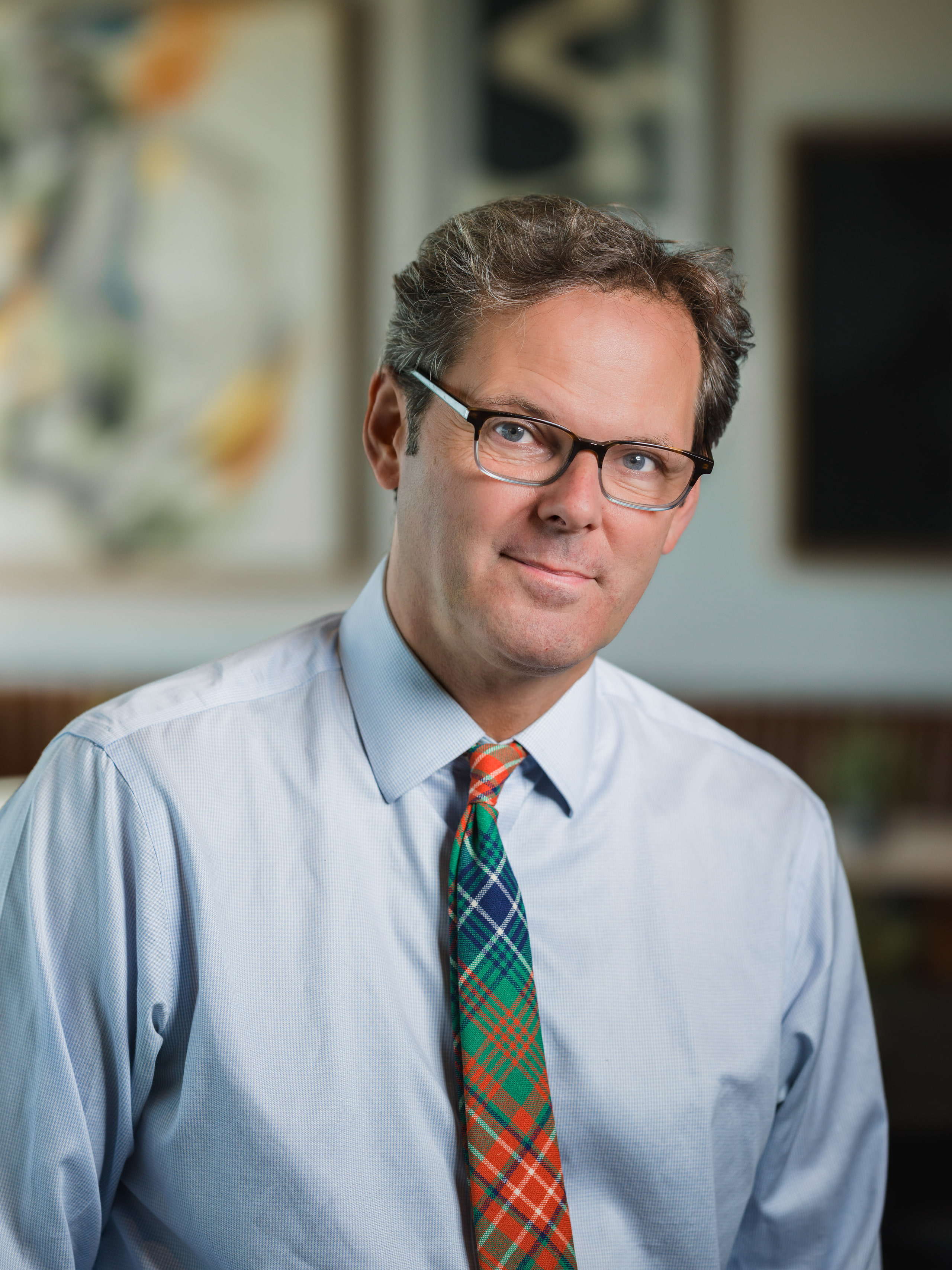 A portrait of a man in glasses and a plaid tie in a coworking lounge, from an on-site portrait day in Frederick, Maryland.
