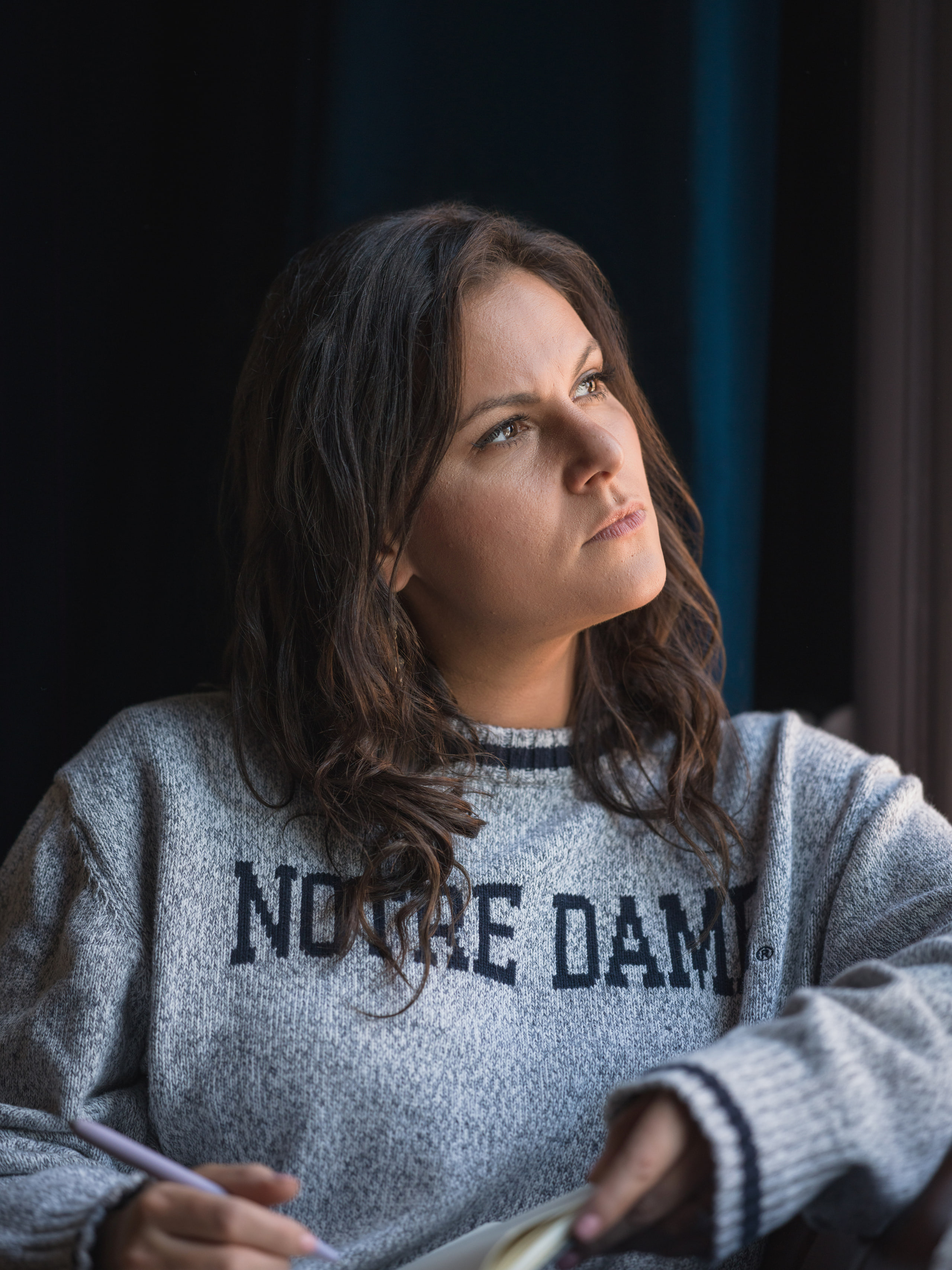 A woman in a sweatshirt with a pen, looking up, at The Exchange on Loudoun.