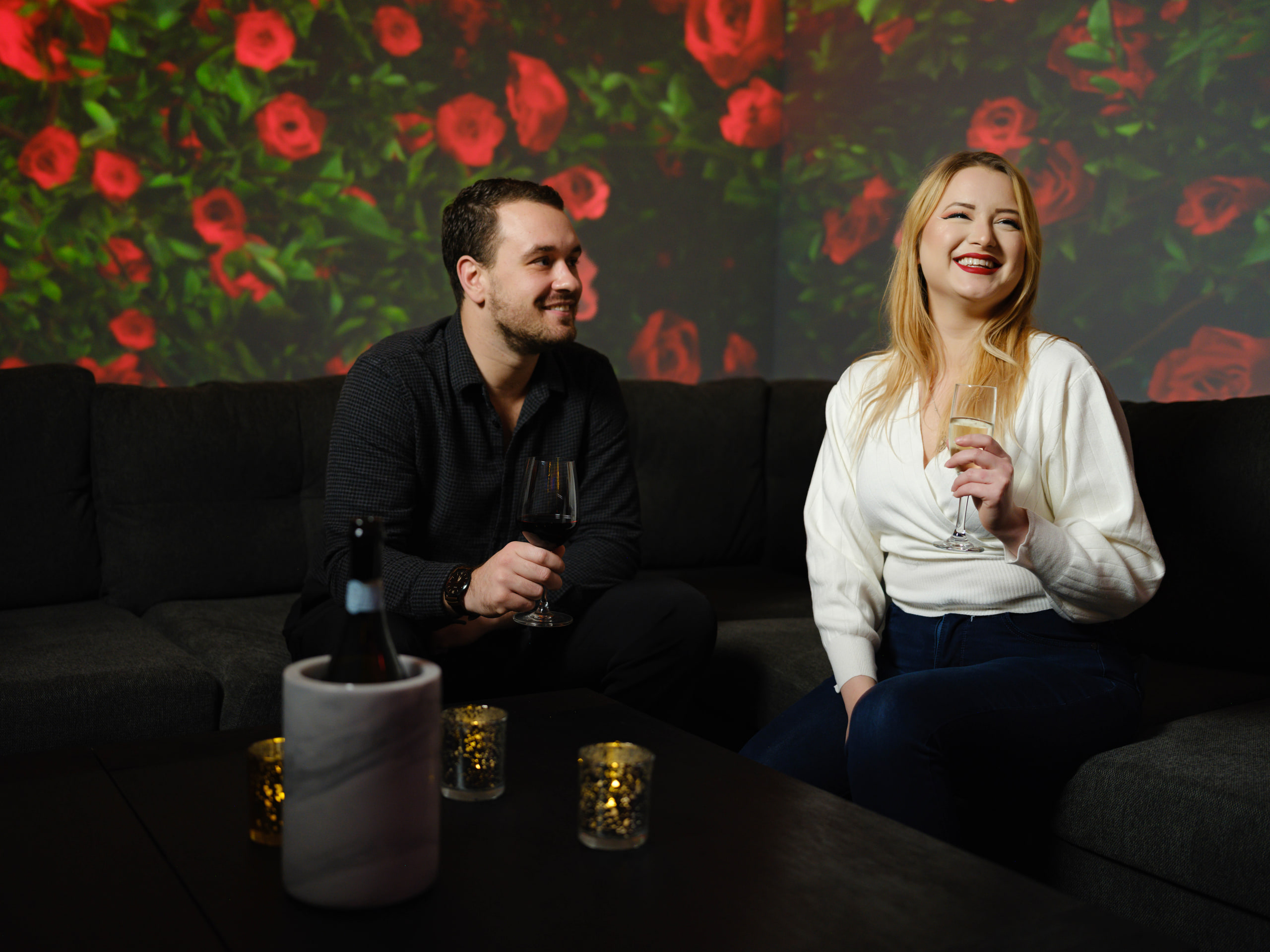 Couple on the couch, roses wall, laughing at a community event.