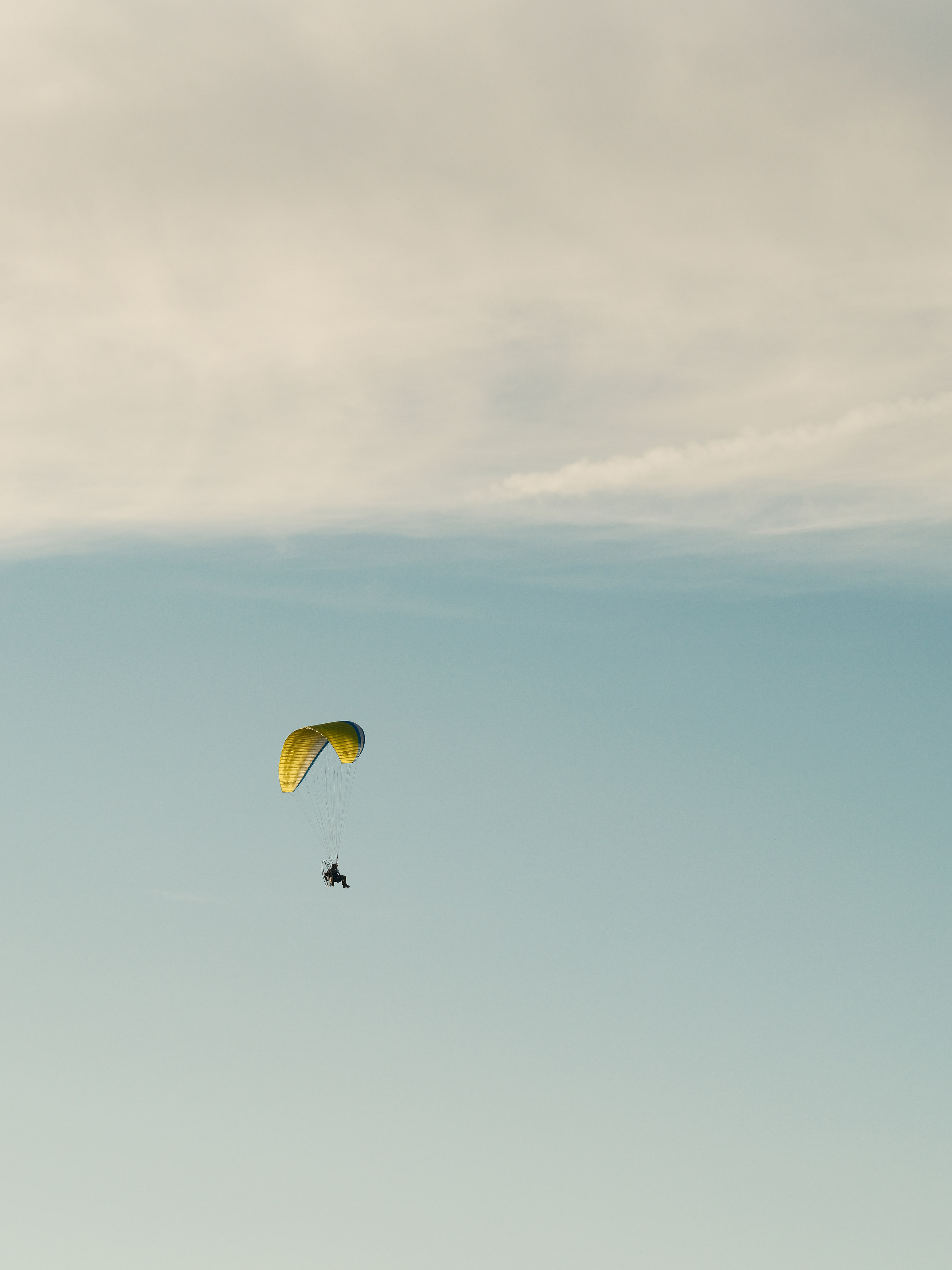 Paraglider alone in a white sky, almost nothing else.