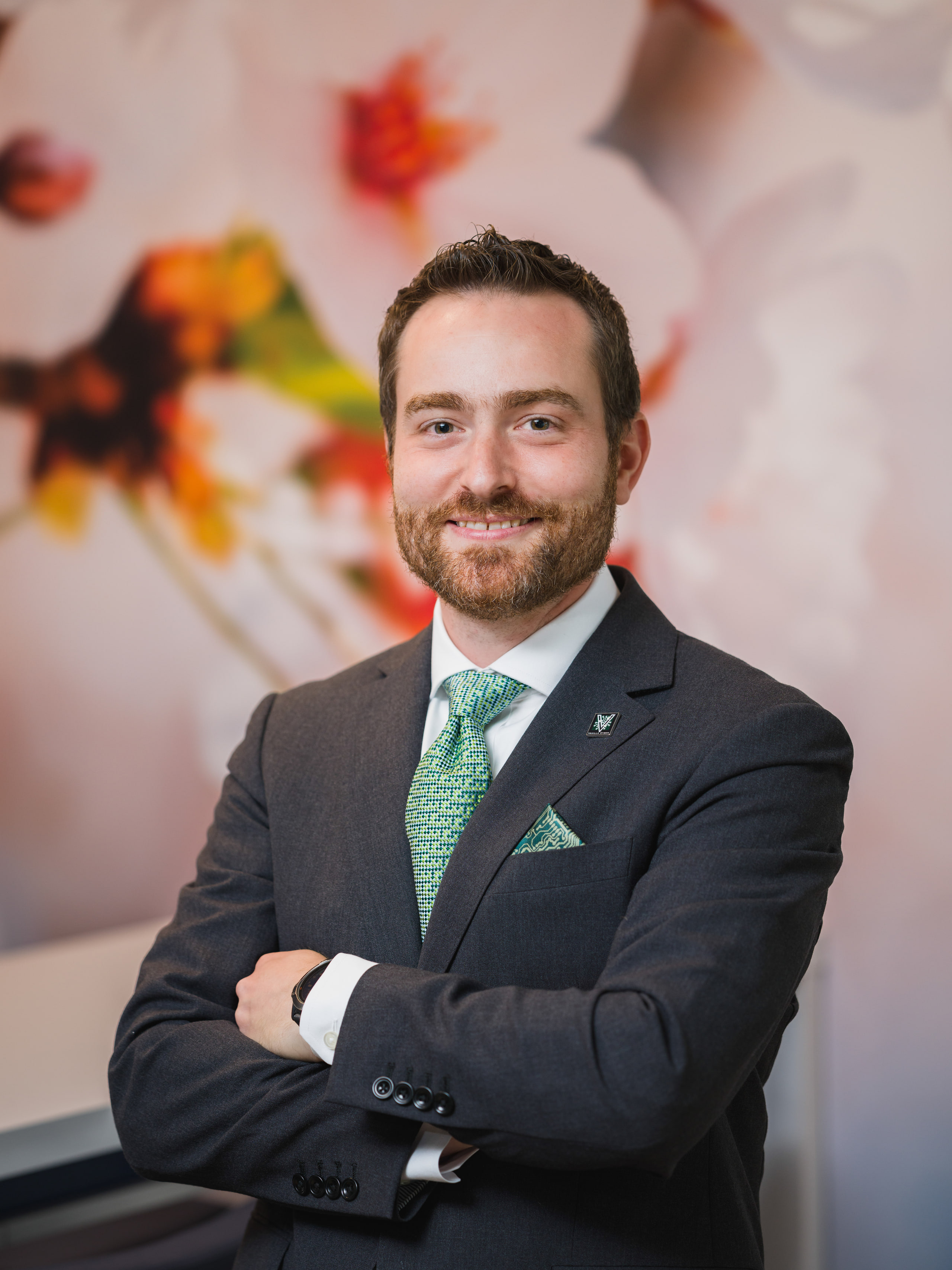 A portrait of a man in a suit and green tie against a cherry-blossom backdrop.