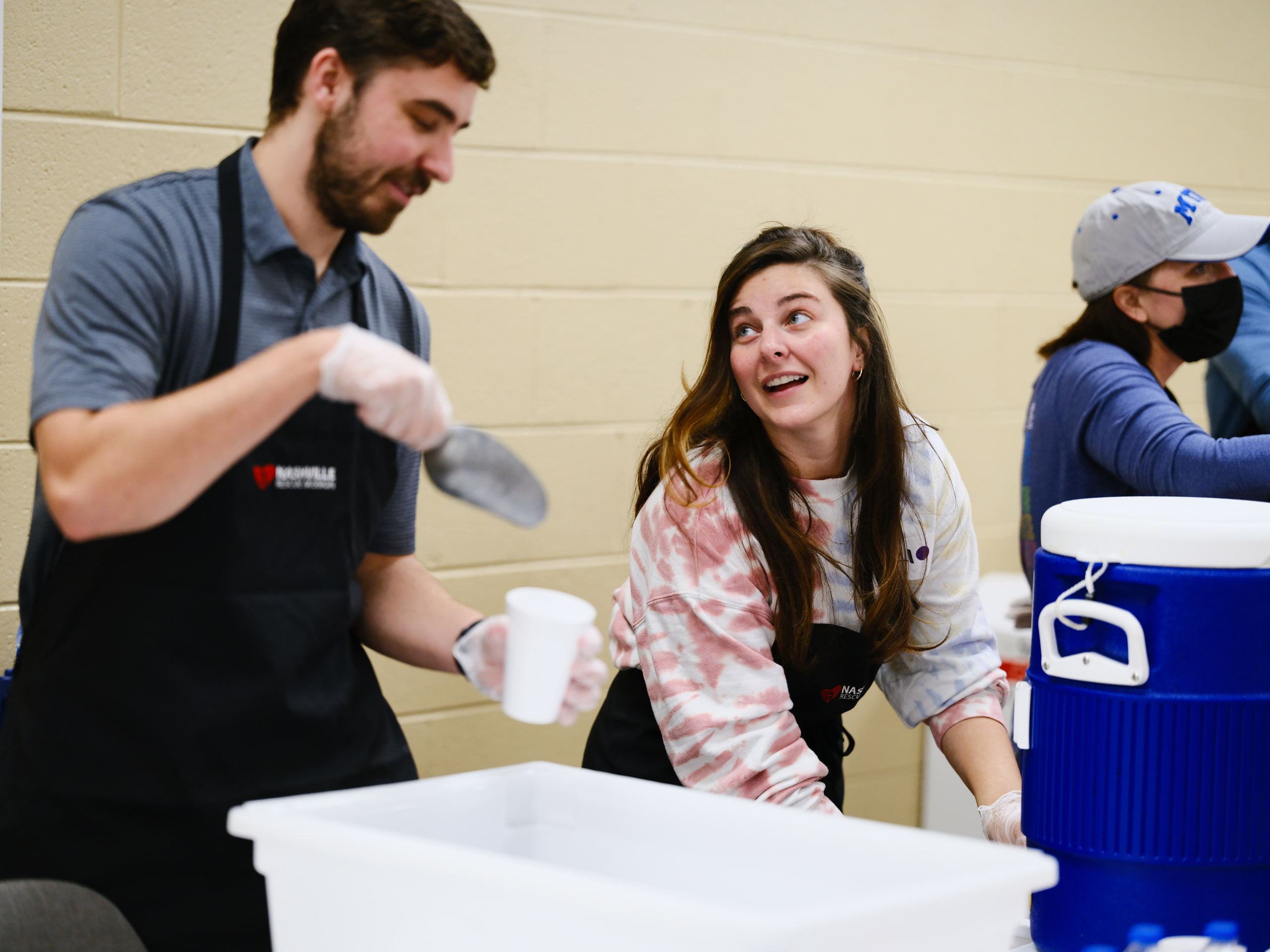 Two volunteers, laughing, wider at a community event.