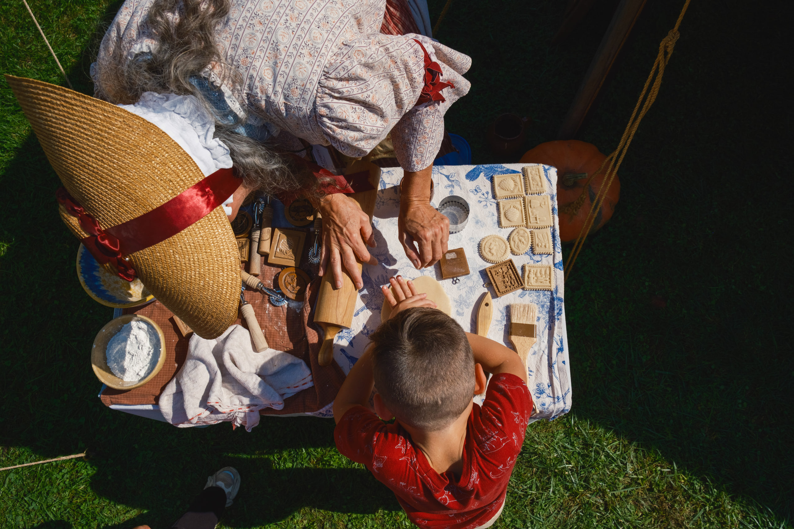 Looking down on a table of wooden cookie molds as a woman in a bonnet and period dress shows a visitor how they work.
