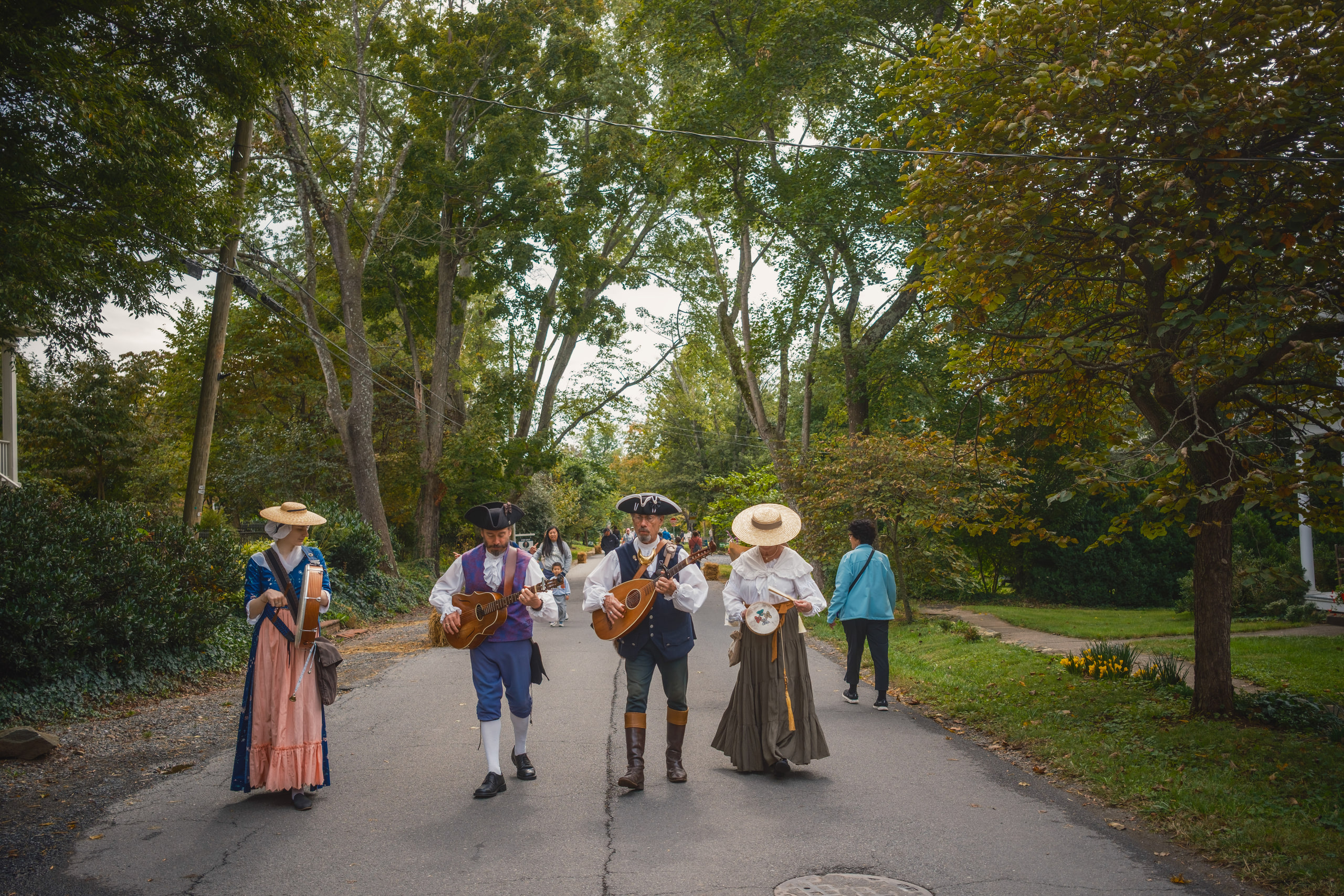 Four musicians in period dress walking down a tree-lined lane at the Waterford Fair, Waterford, Virginia.