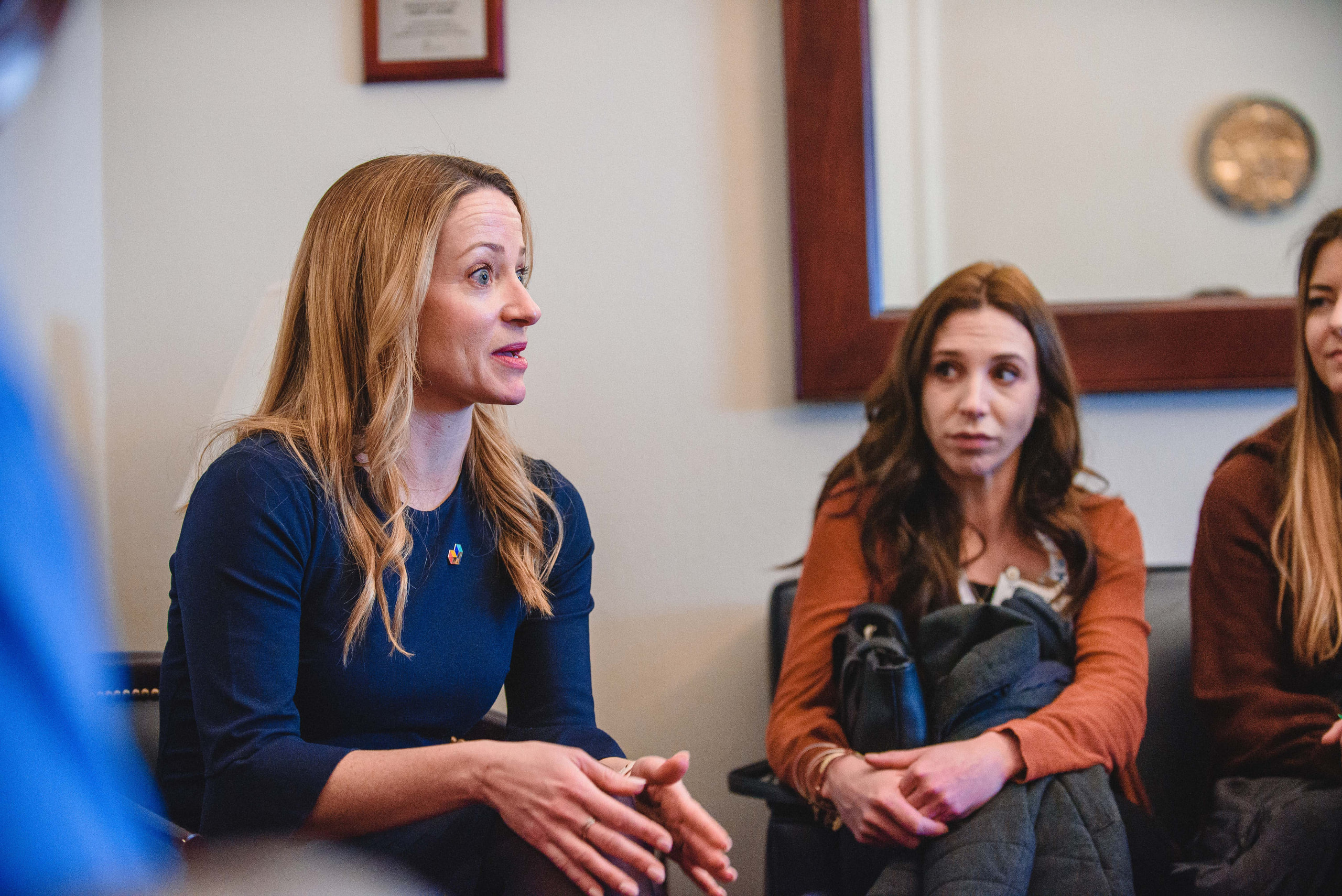 A woman speaking from a couch in a small conference session, another attendee listening beside her.