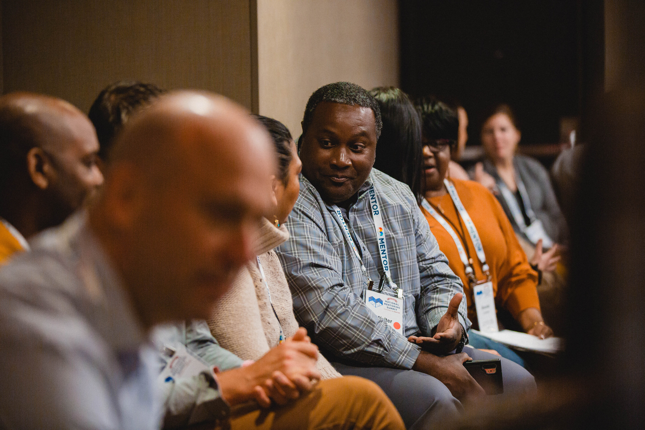 Conference attendees with lanyards laughing in conversation around a table, warm light.