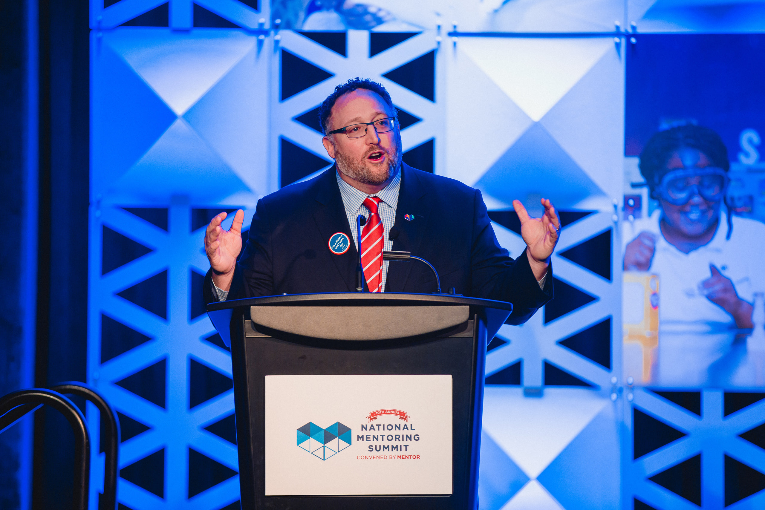 Speaker at the podium, red tie, animated at a conference in Washington, DC.