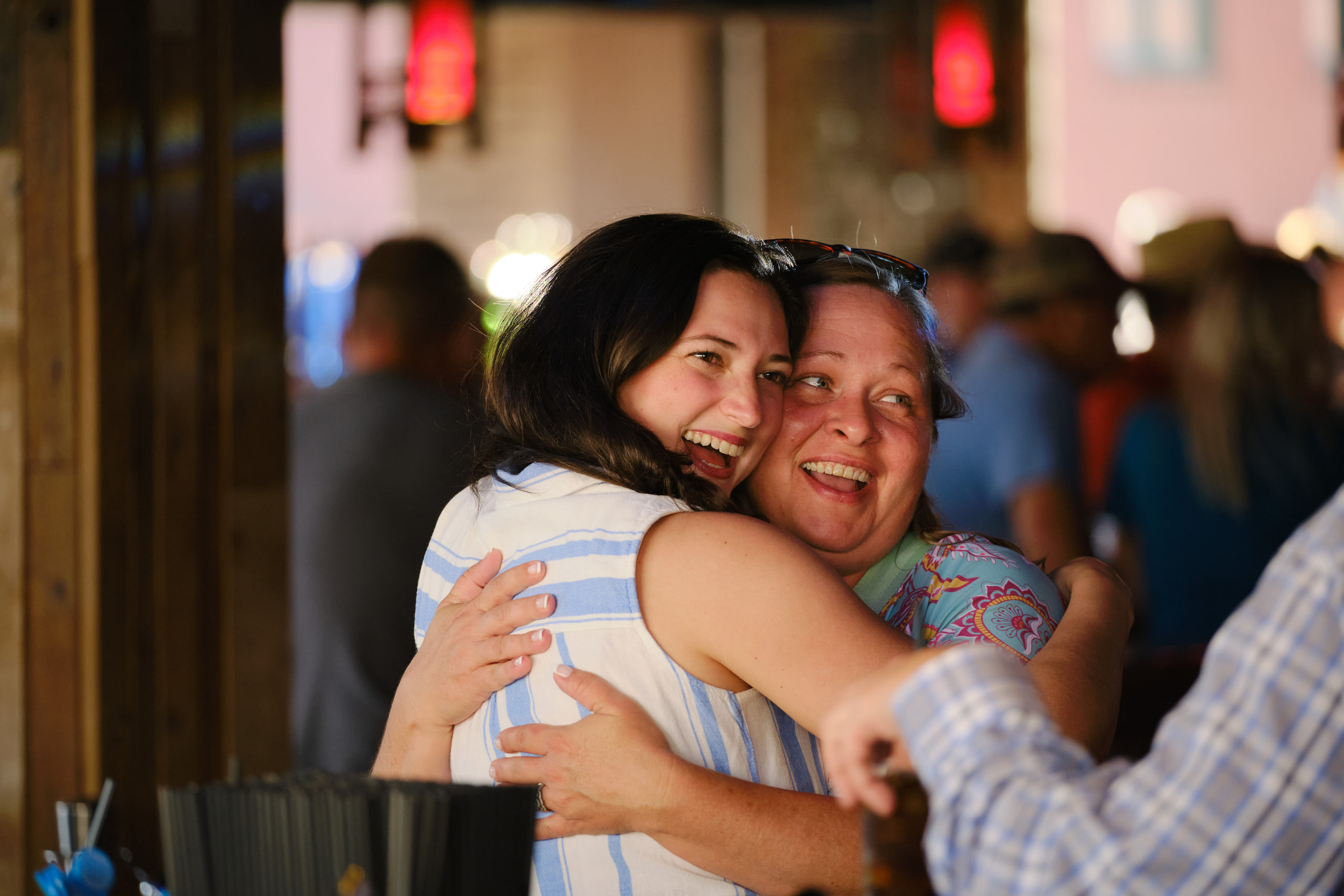 Two women hugging, laughing, warm at a rooftop industry mixer, Nashville.