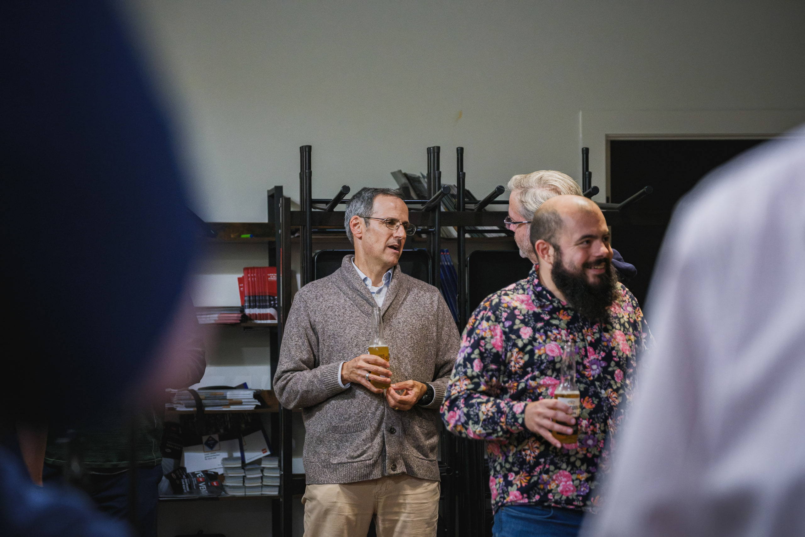 Guests stand talking with drinks in hand beside metal shelving before an evening panel.