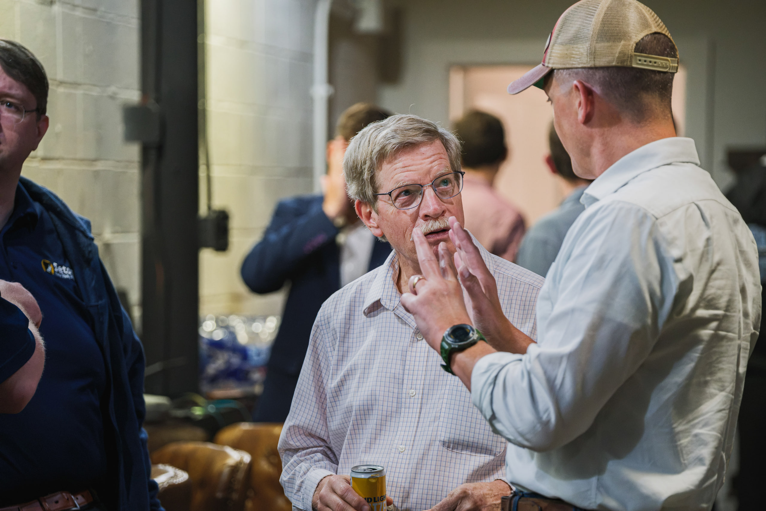 Two men laugh in conversation after an evening panel, one gesturing with both hands, a can in his other hand.