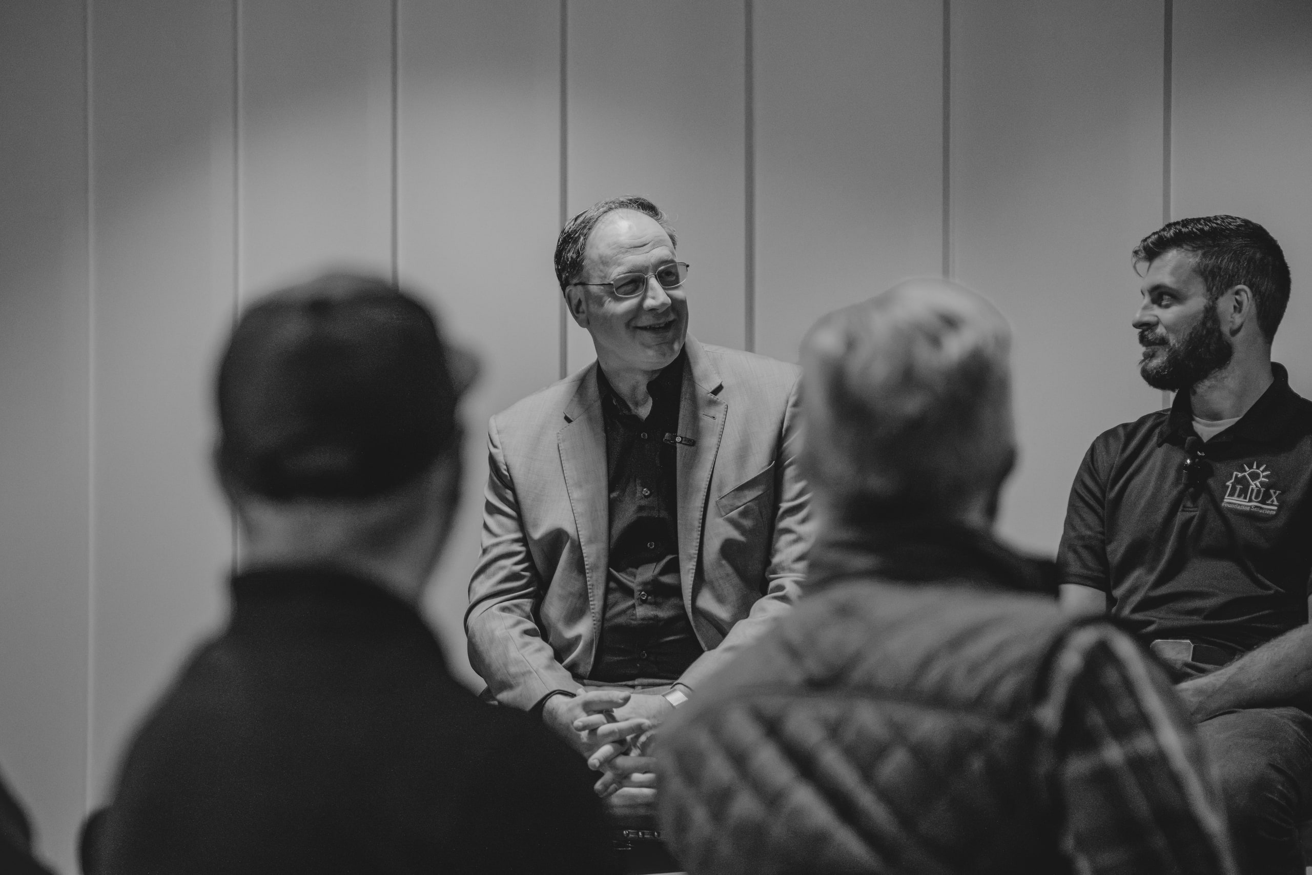 Black and white: two panelists smile at the audience, seen past listeners in the foreground.