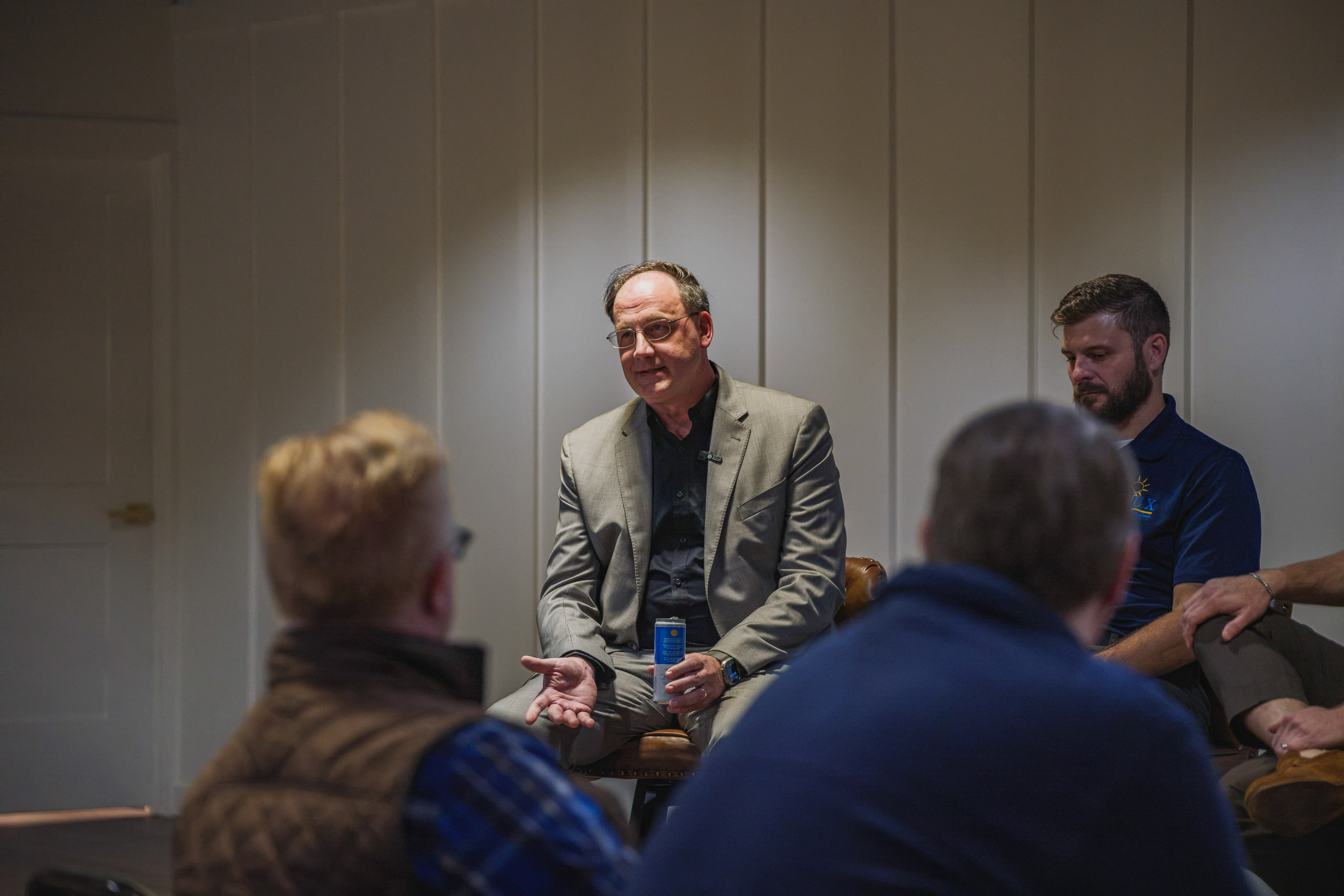 A speaker in a gray blazer smiles mid-answer, another panelist beside him and the audience in the foreground.