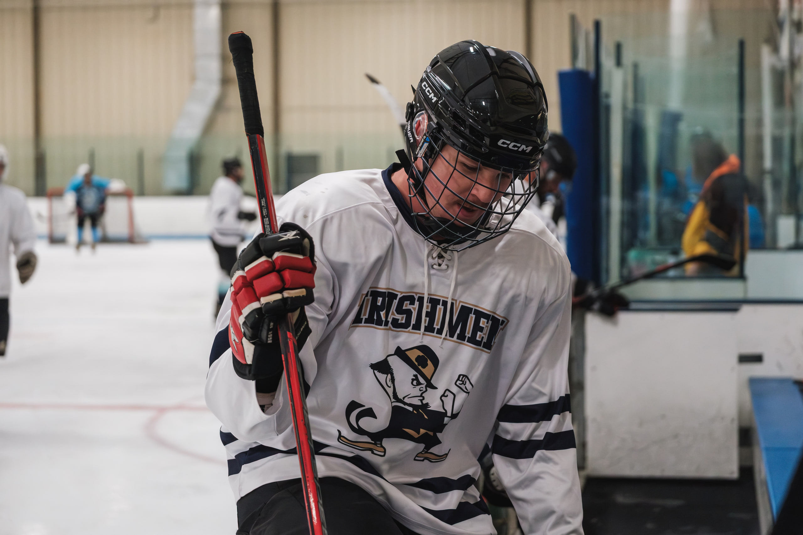 A hockey forward in white leaning into the frame, face in the cage.