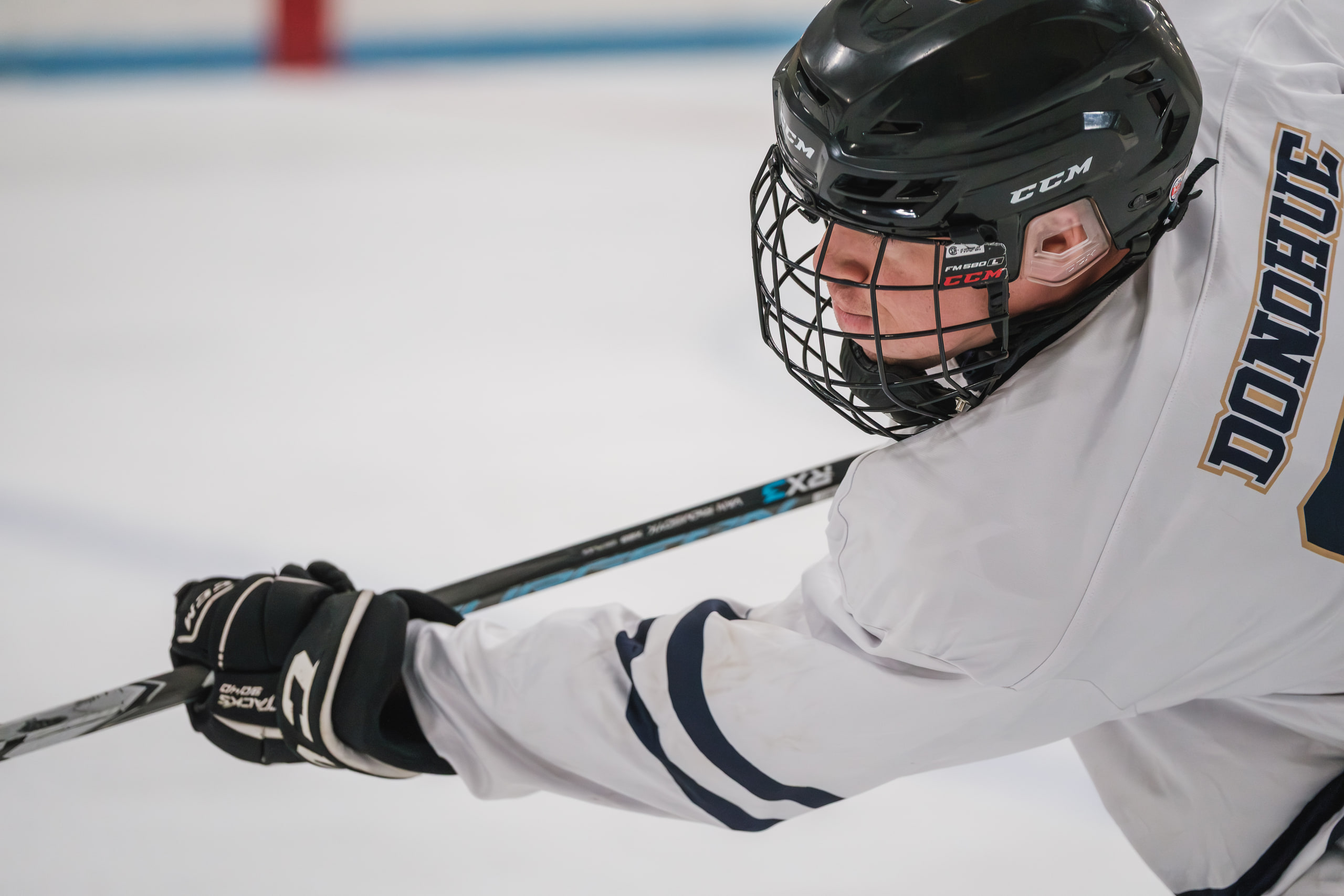 A hockey player close, stick across the frame, helmet on.