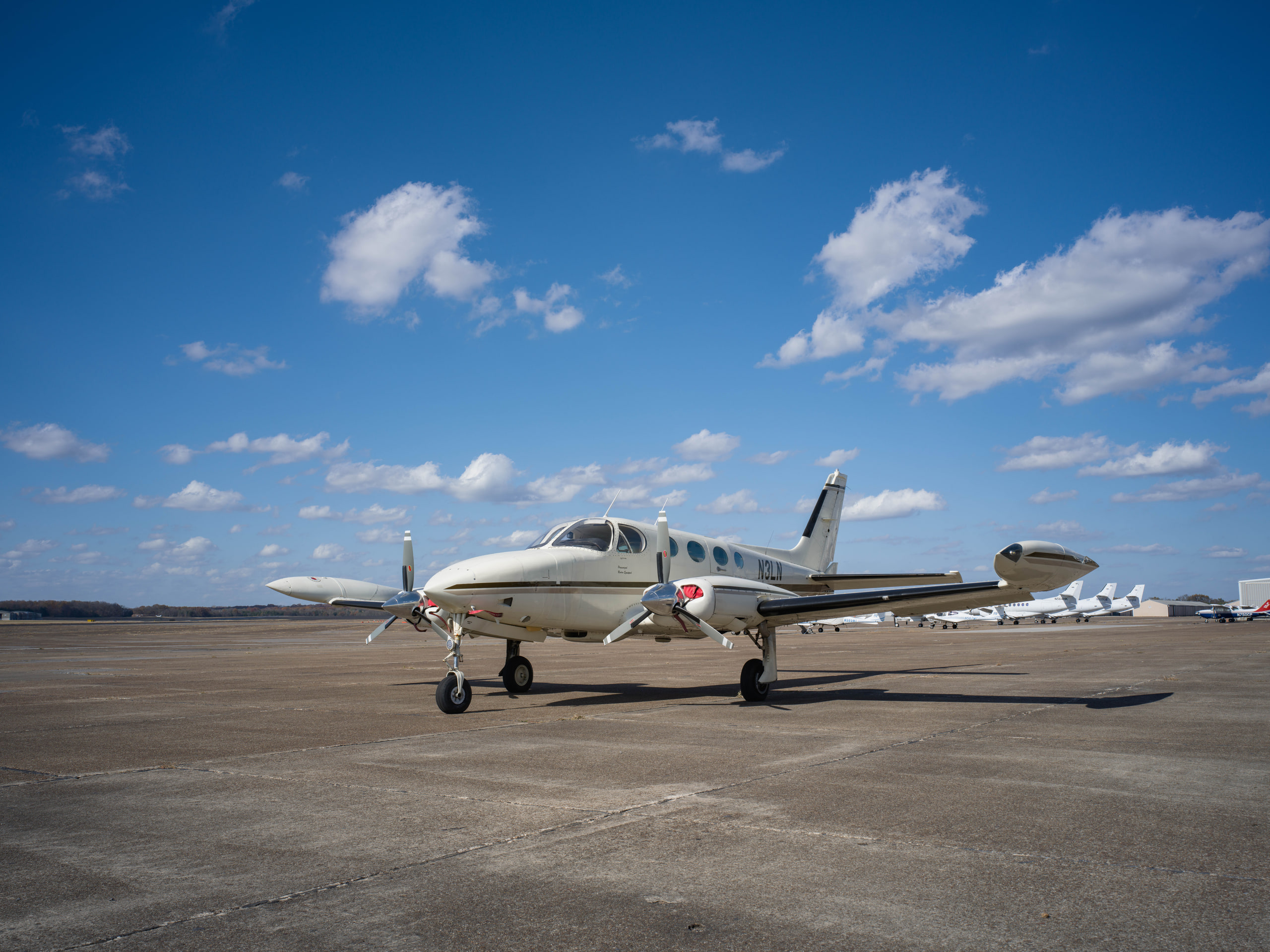 Twin head-on under clouds, wide at an aviation maintenance company.