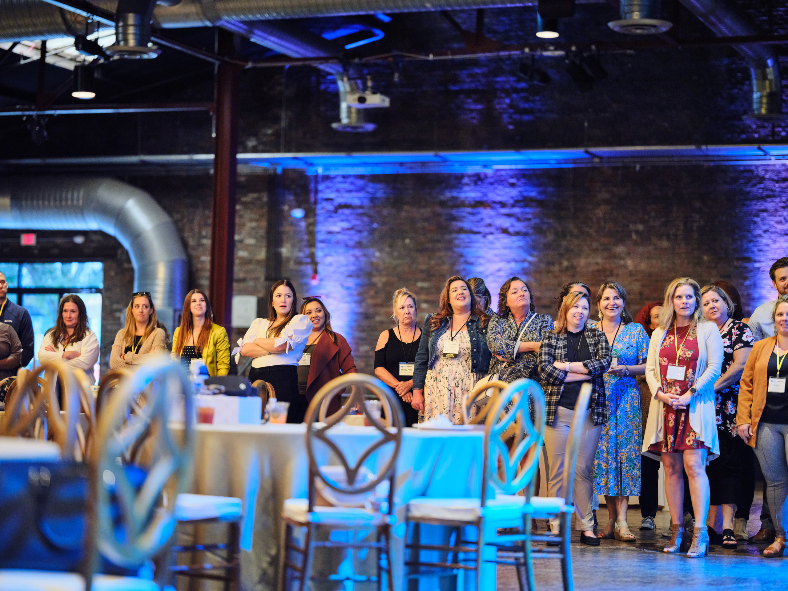 The crowd standing, blue-lit brick at a team-building event in a brick warehouse venue, Nashville.