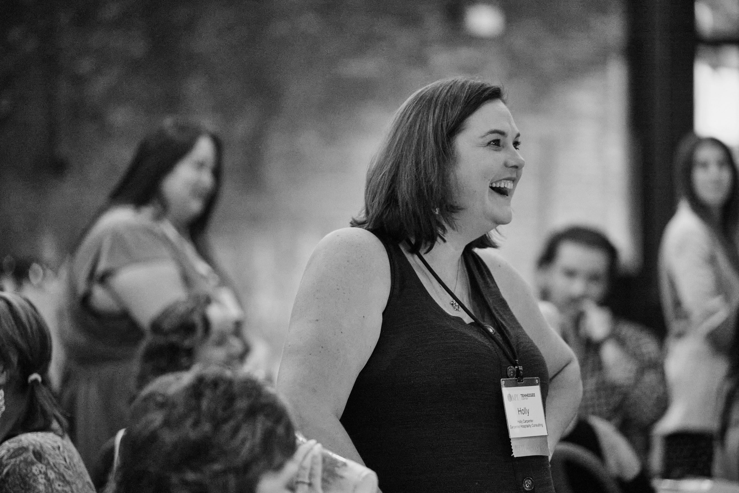 Black and white woman laughing in the crowd at a team-building event in a brick warehouse venue, Nashville.