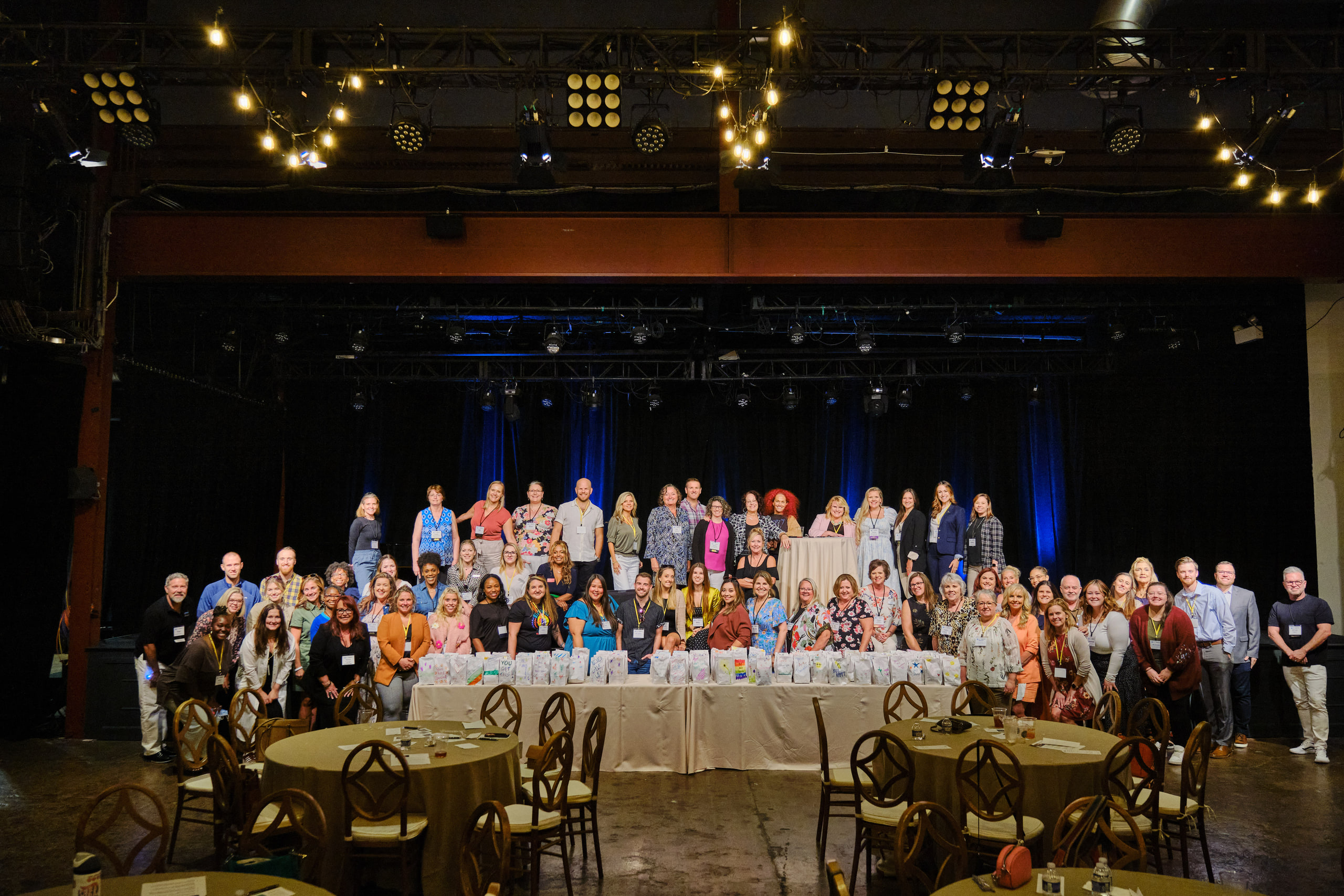 The whole group on stage, hands up at a team-building event in a brick warehouse venue, Nashville.