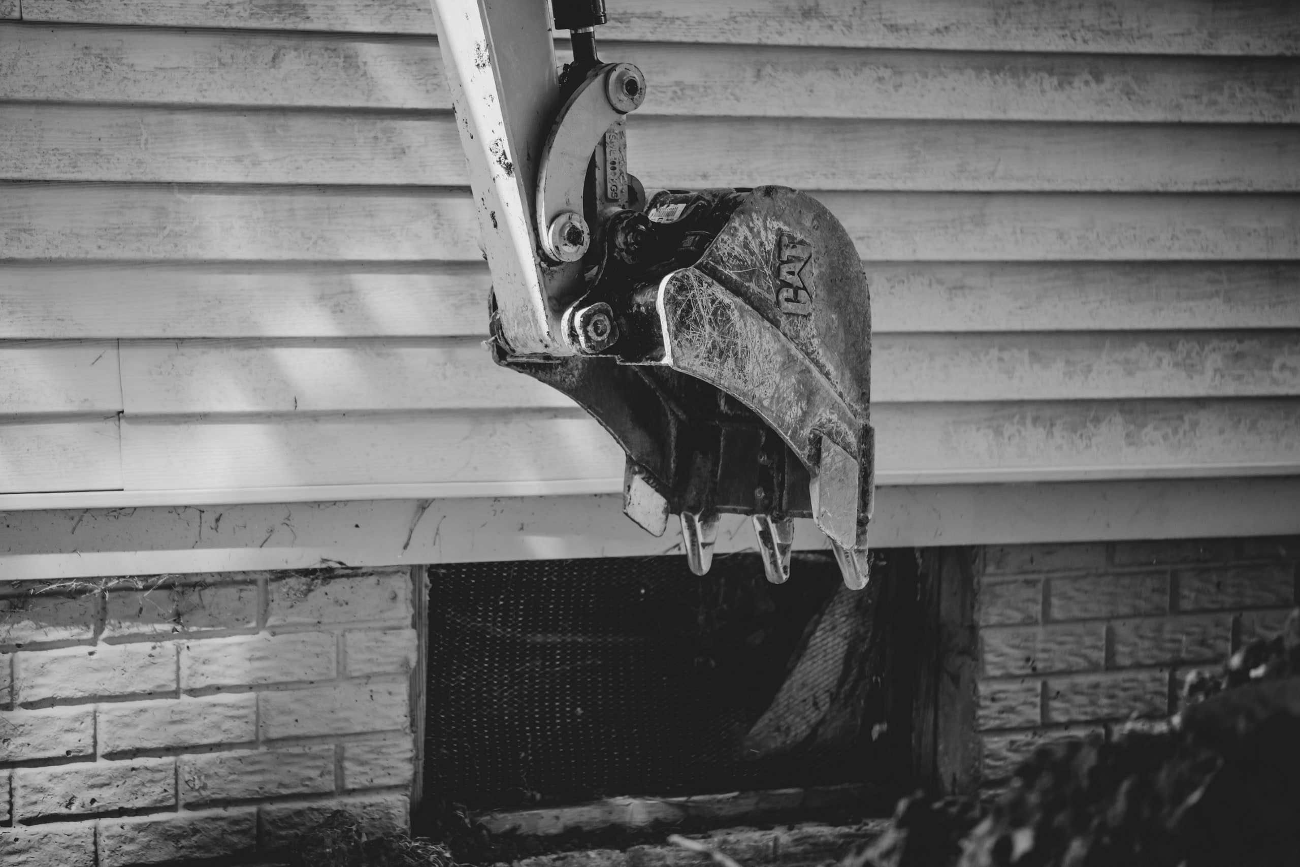 An excavator bucket against house siding, black and white.