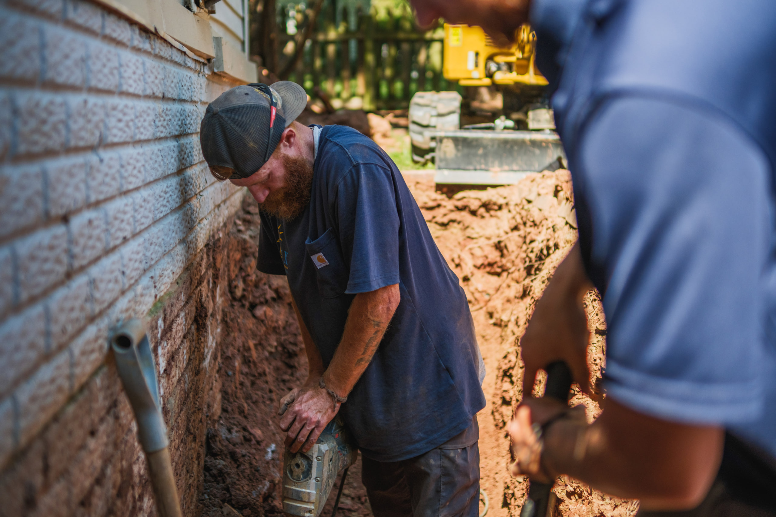 A foundation repair crew working in a trench beside a house.
