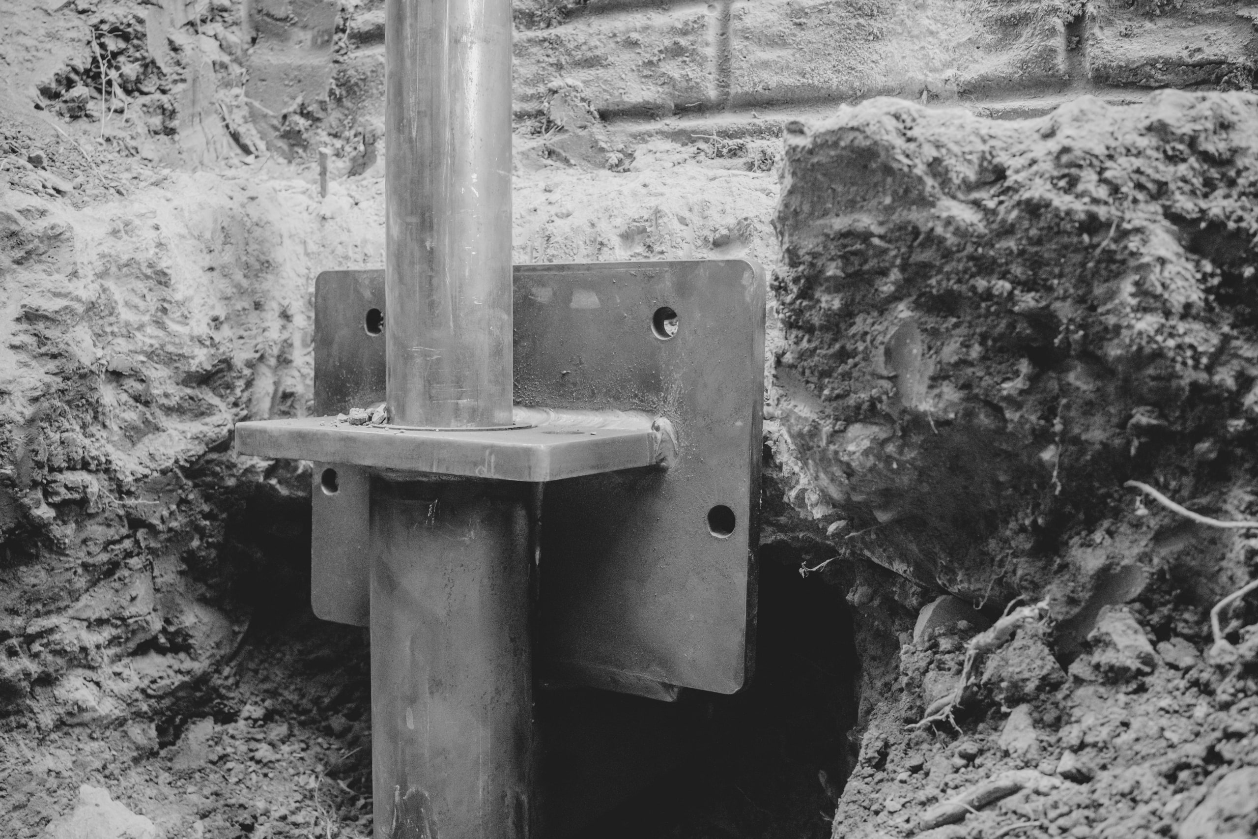 A steel pier bracket set under a house footing, black and white.