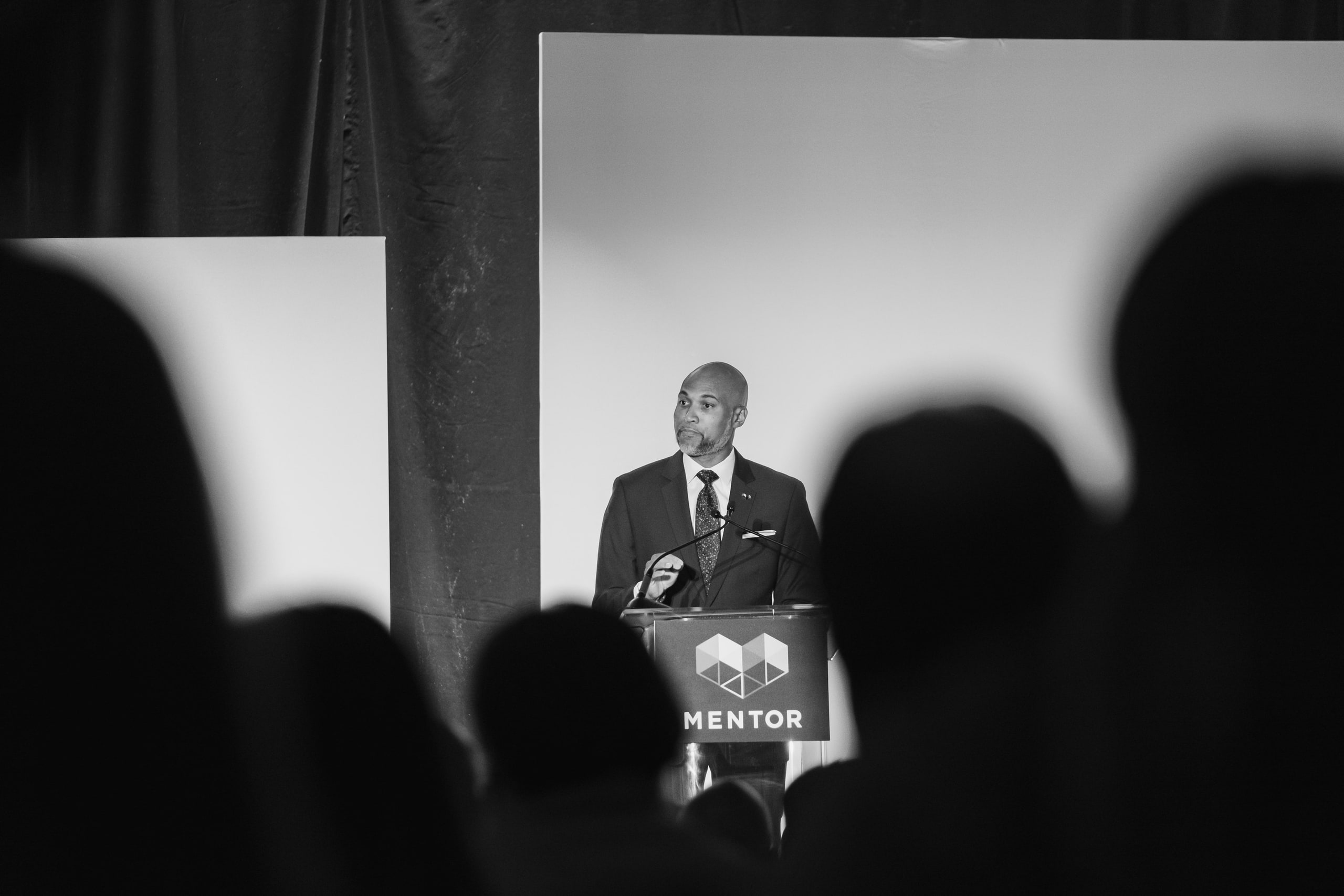 Black and white speaker between silhouettes at a national summit plenary.