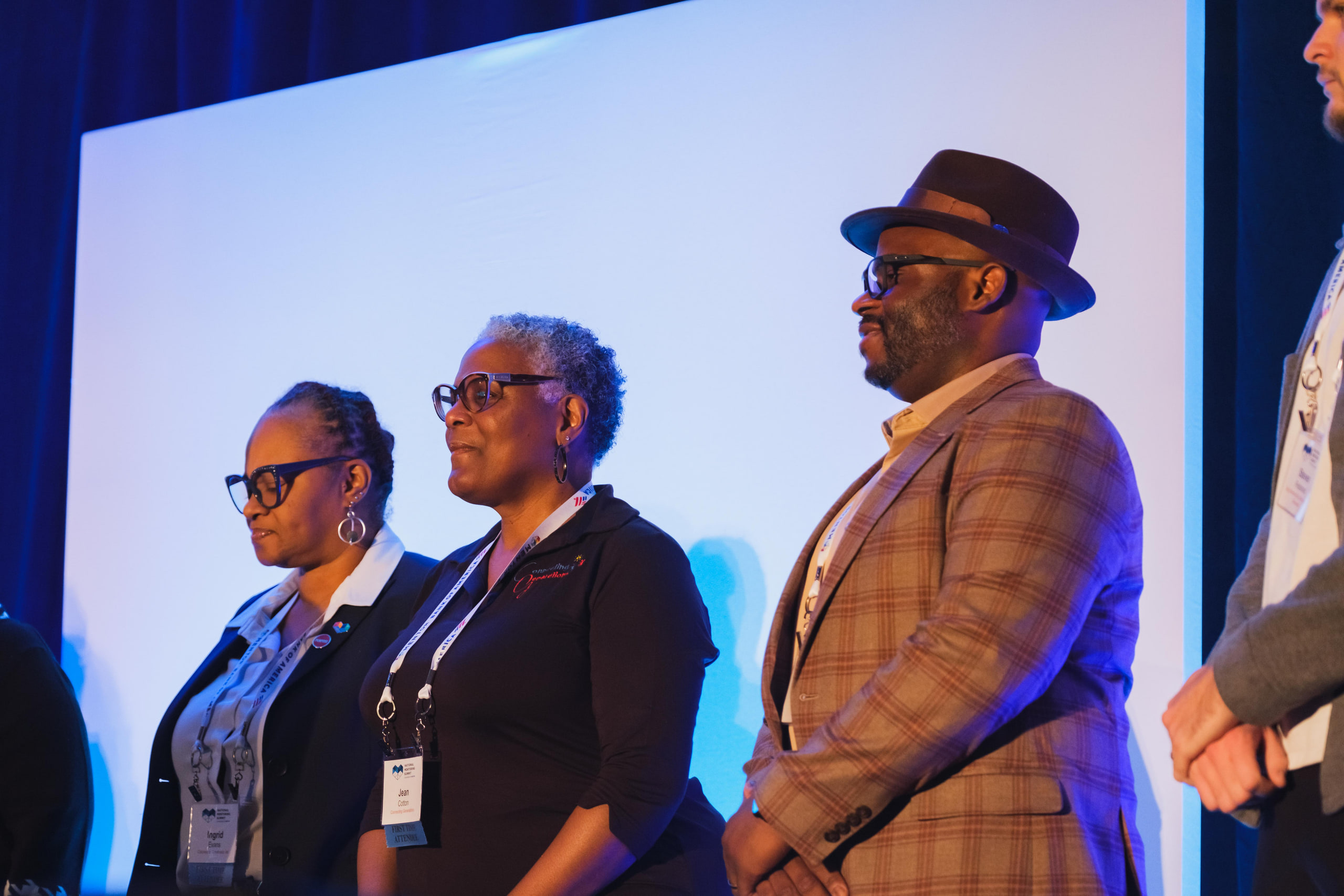 Three on stage, hat and glasses, warm at a national summit plenary.