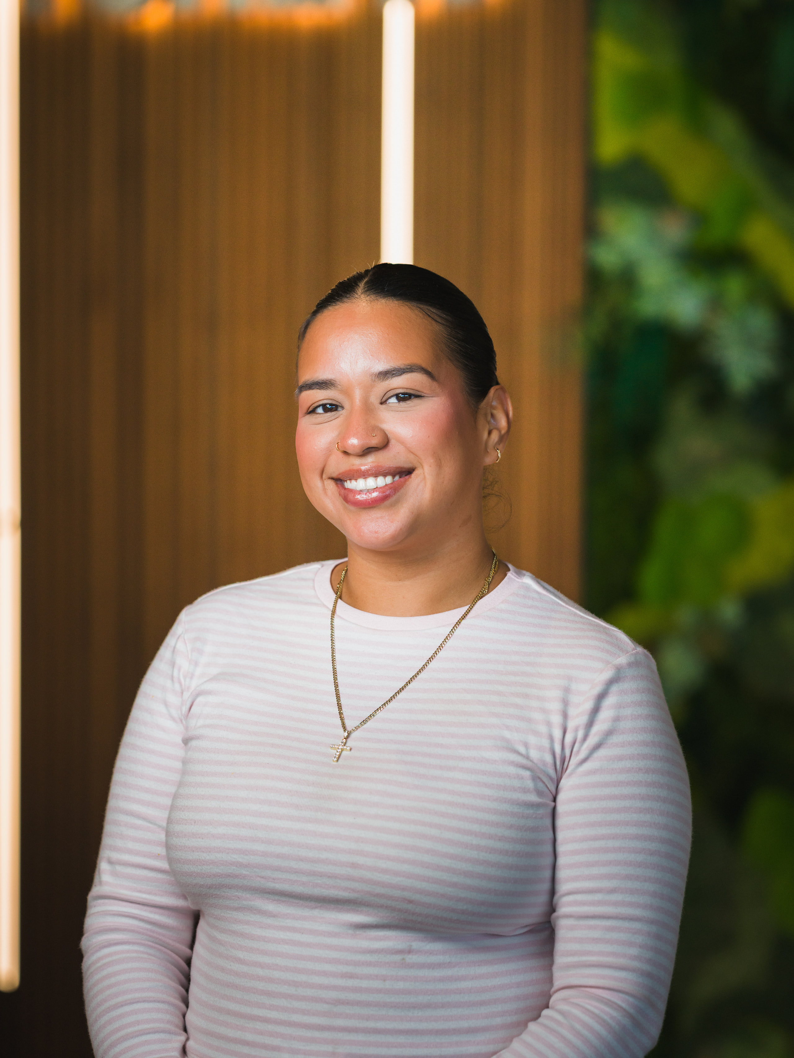 A portrait of a woman in a white top with a living wall and neon behind her, from a coworking portrait day.