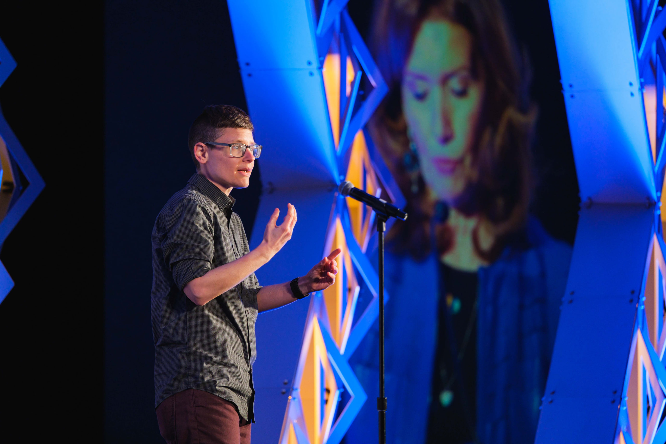 Speaker gesturing through a blurred foreground at a national summit opening plenary.