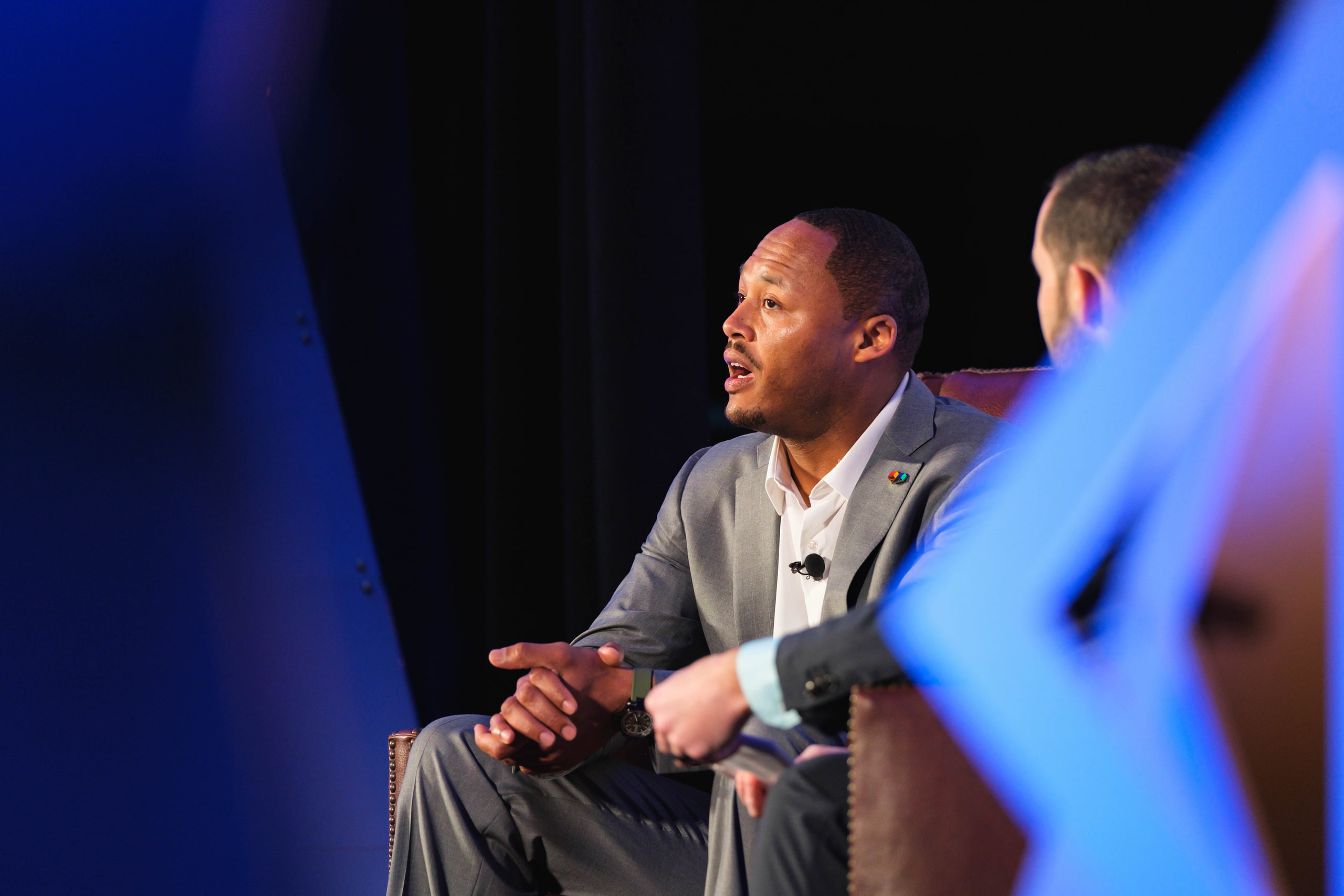 Gray suit talking in the chair, blue at a national summit opening plenary.