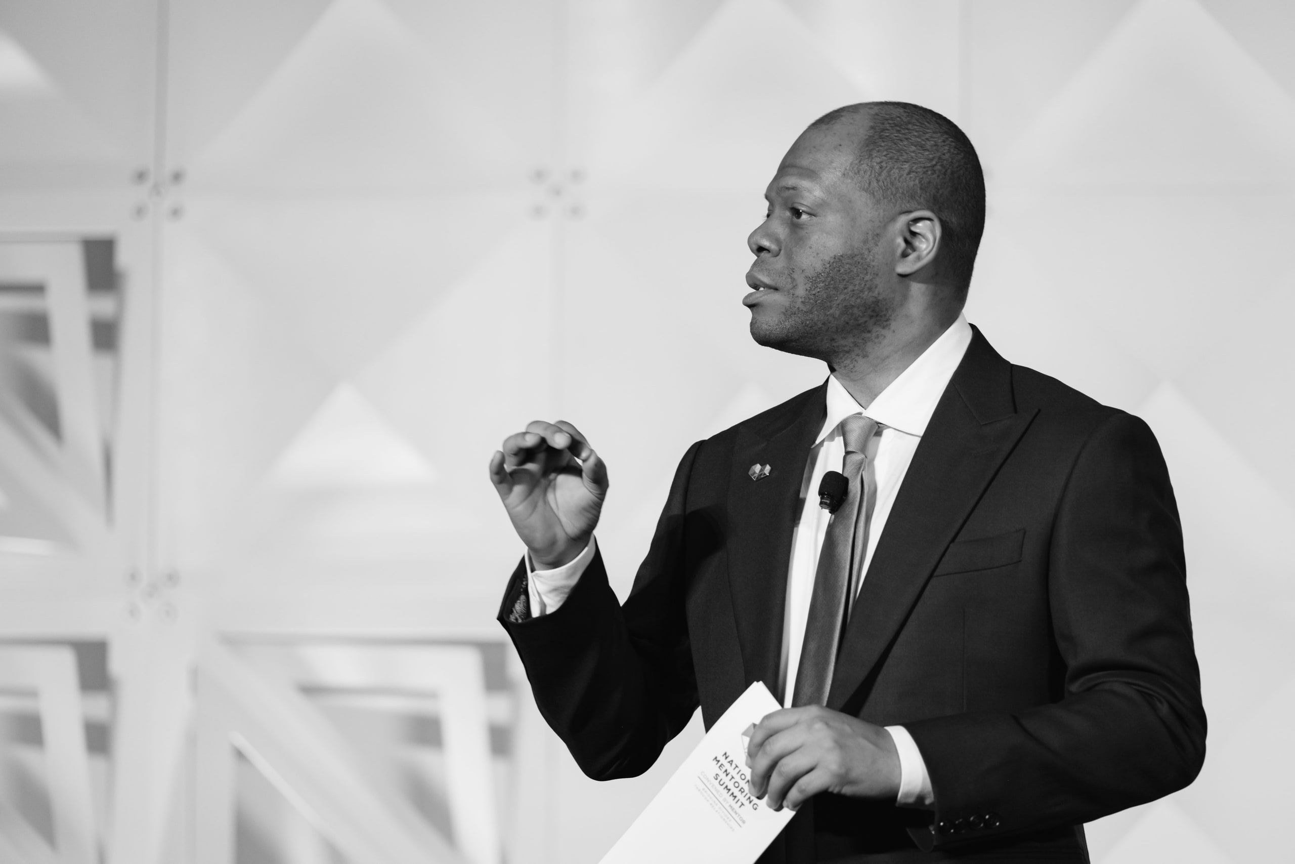 Black and white speaker mid-gesture at a national summit opening plenary.