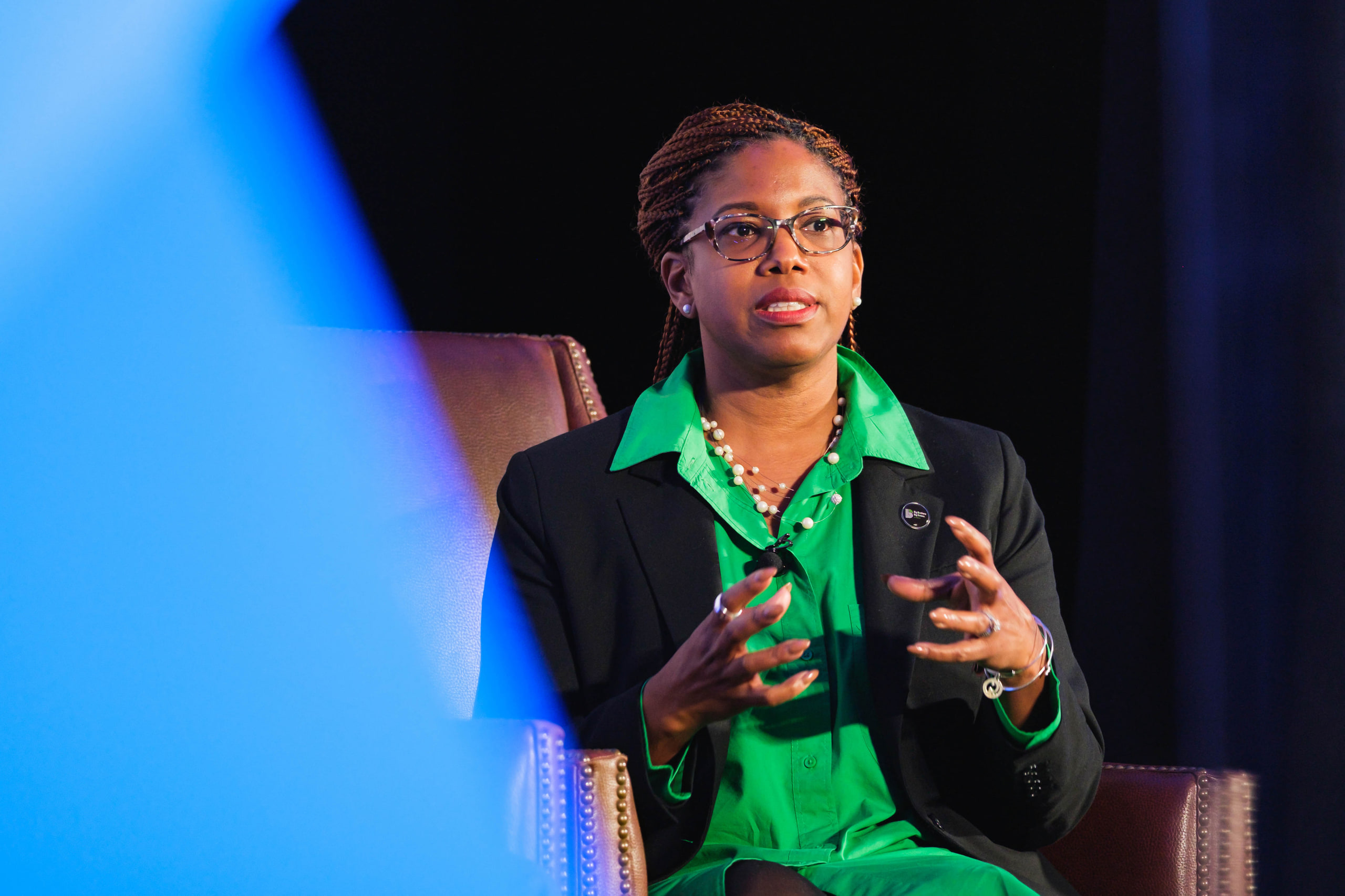 Green blouse gesturing, blue at a national summit opening plenary.